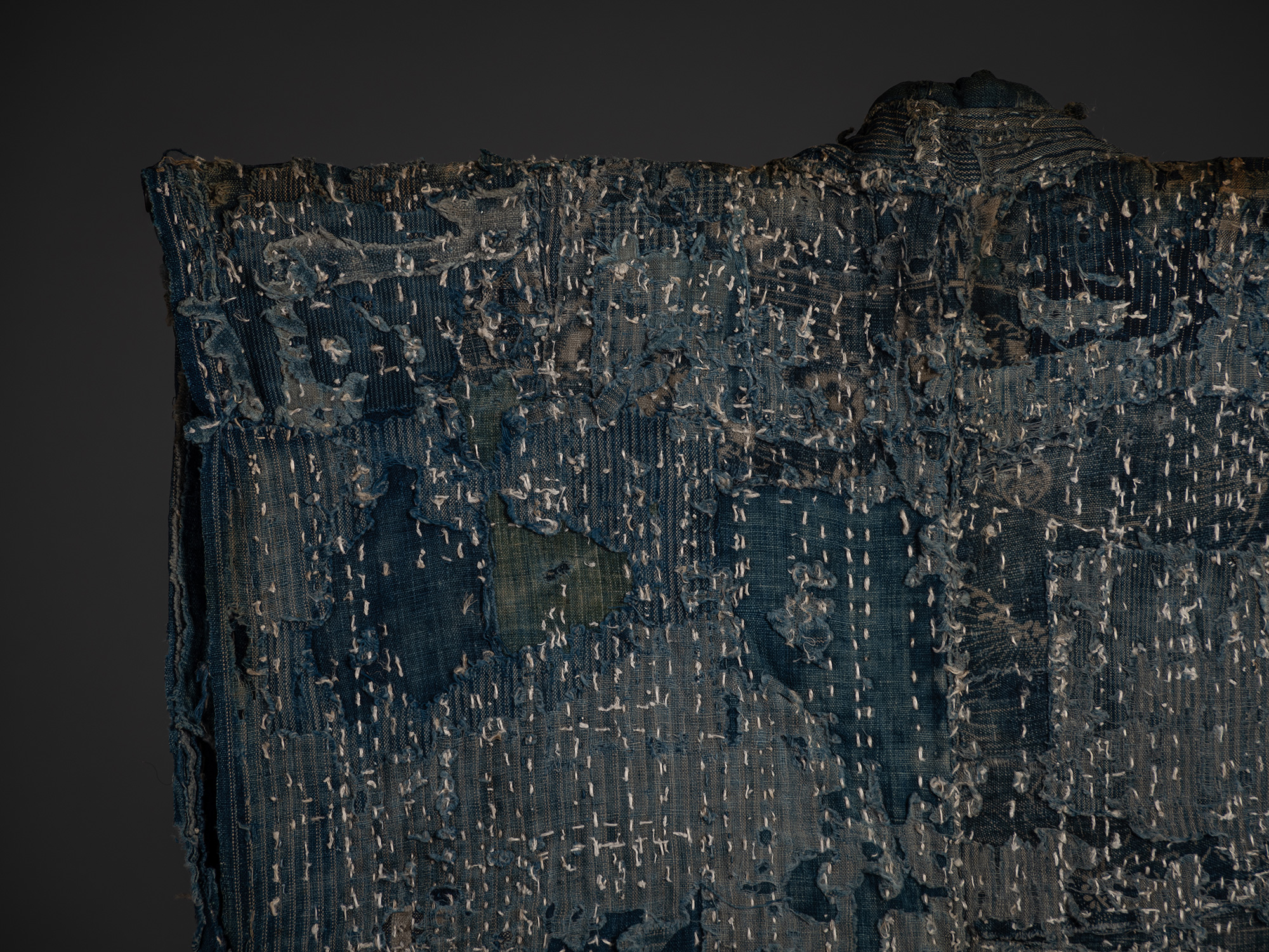 Close-up of the upper back of the boro work coat showing overlapping indigo cotton and hemp patches...