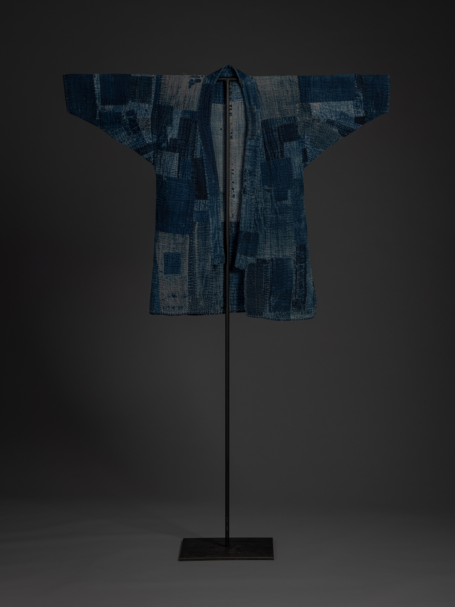 Full front view of a Japanese boro work coat displayed on a stand. The indigo-dyed garment is assembled...