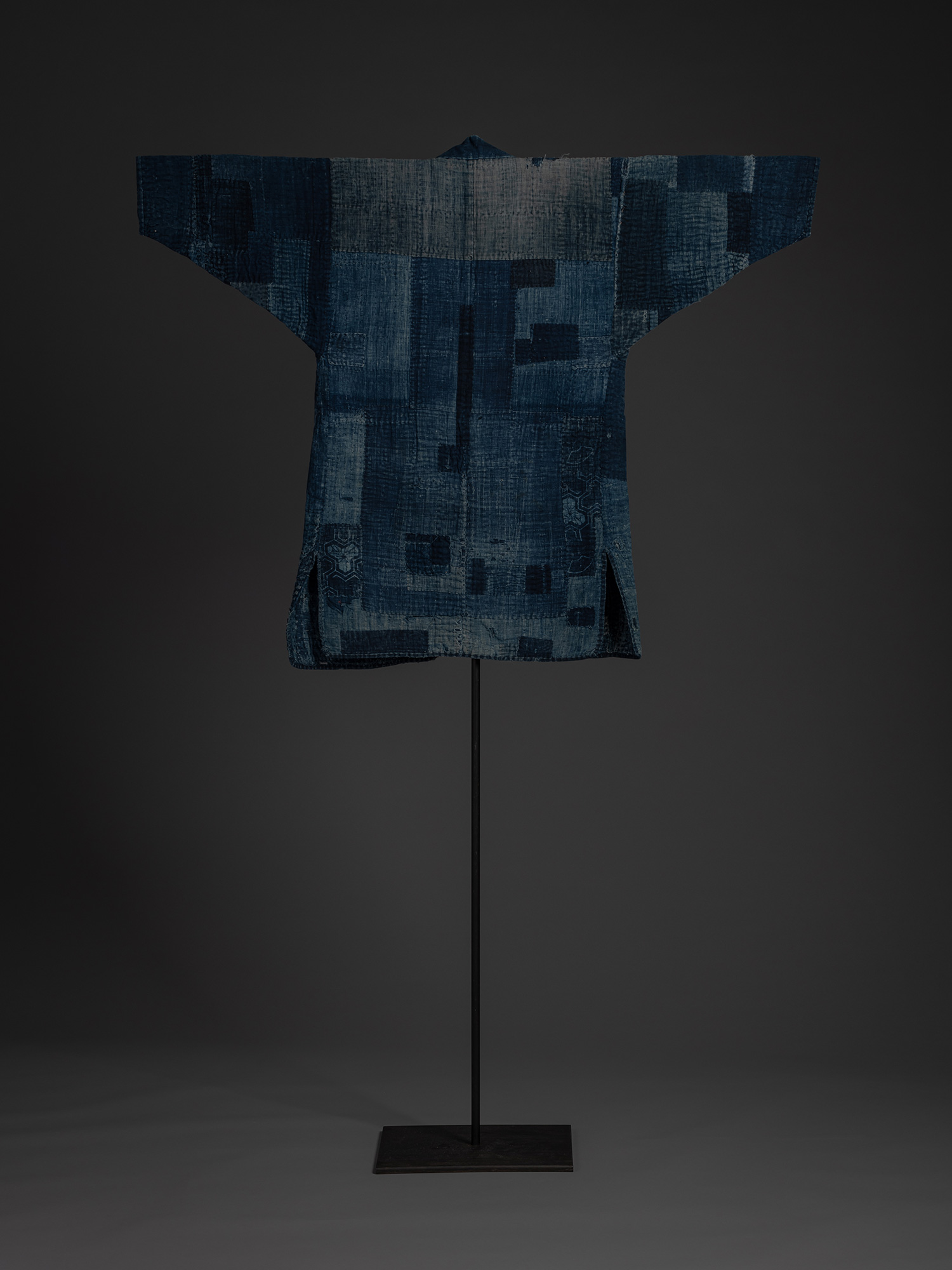 Full back view of a Japanese boro work coat displayed on a stand. The broad back panel is composed...