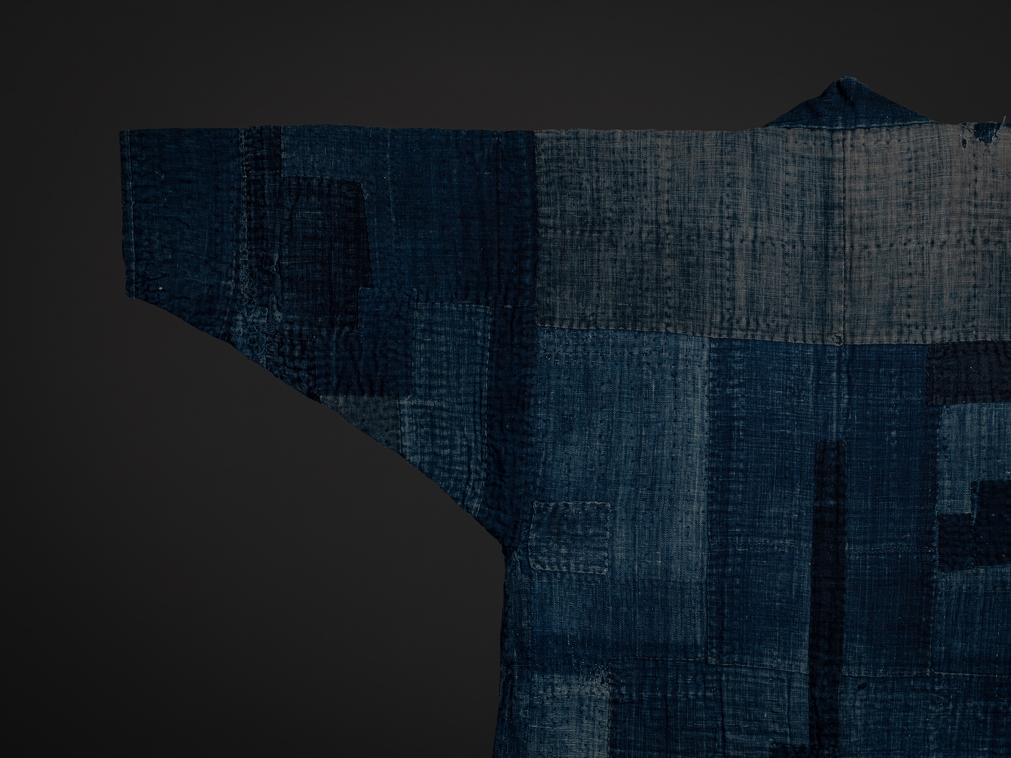 Close-up of the left shoulder and sleeve of the boro work coat, highlighting layered indigo textile...