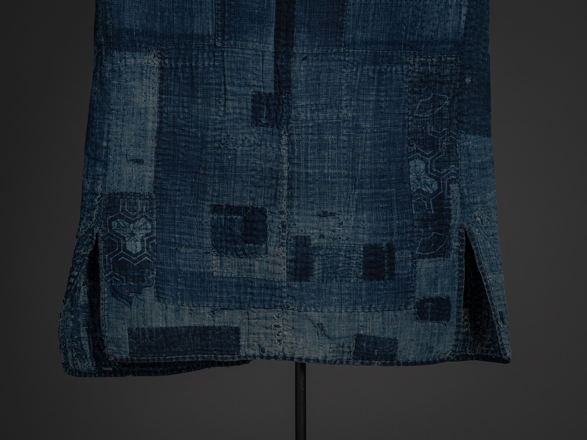 Close-up of the lower back of a Japanese boro work coat, showing a dense patchwork of indigo-dyed...
