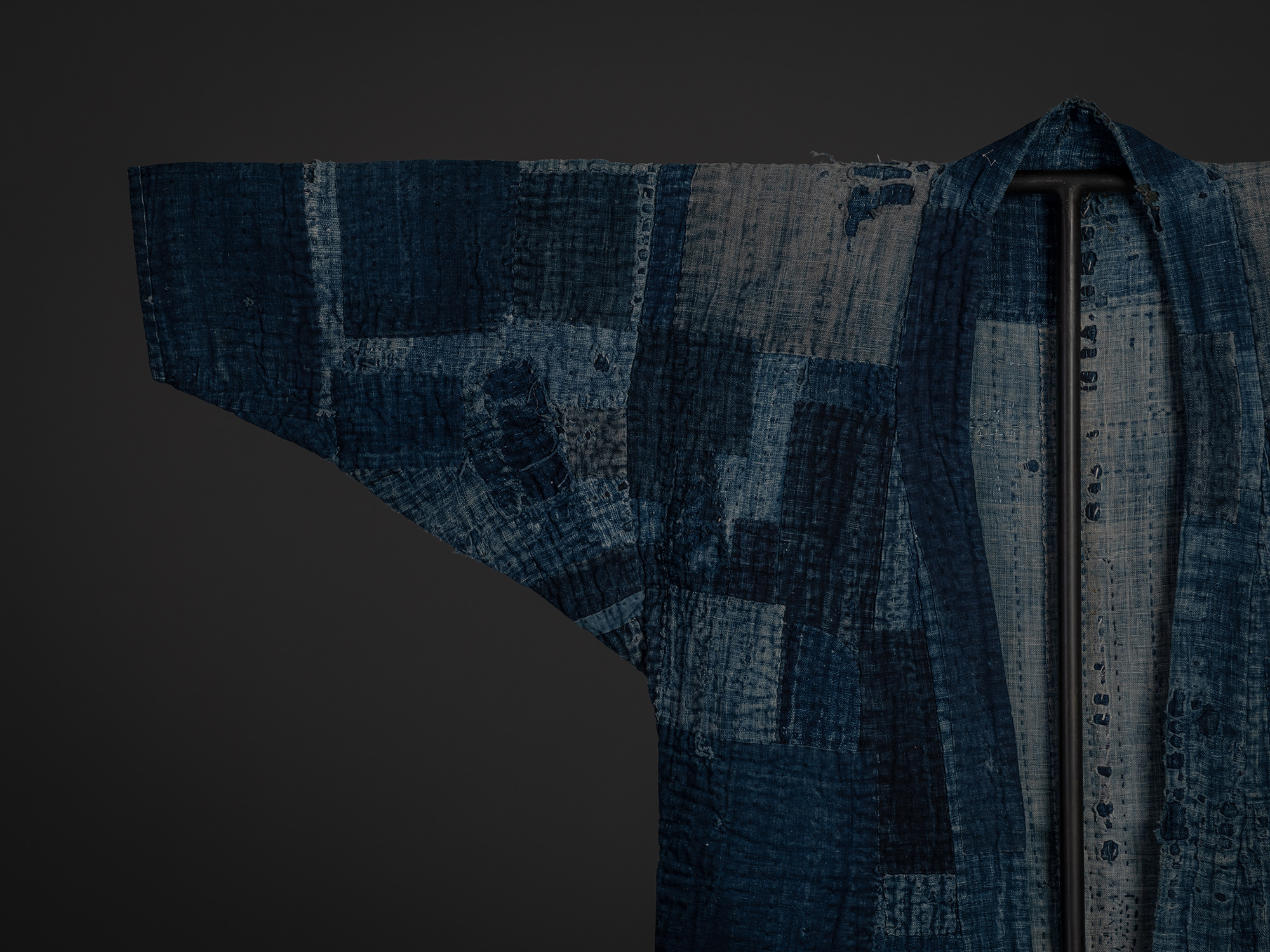 Close-up of the left shoulder and sleeve of a Japanese boro work coat, showing overlapping indigo-dyed...