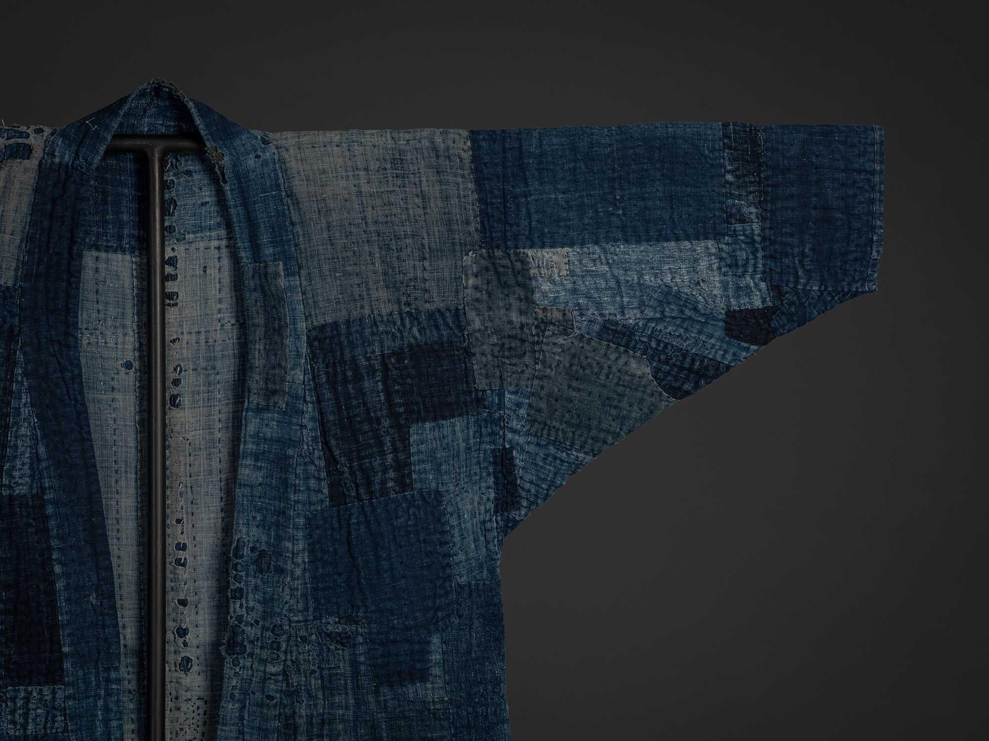 Close-up of the right shoulder and sleeve of the boro work coat, highlighting a patchwork of indigo...
