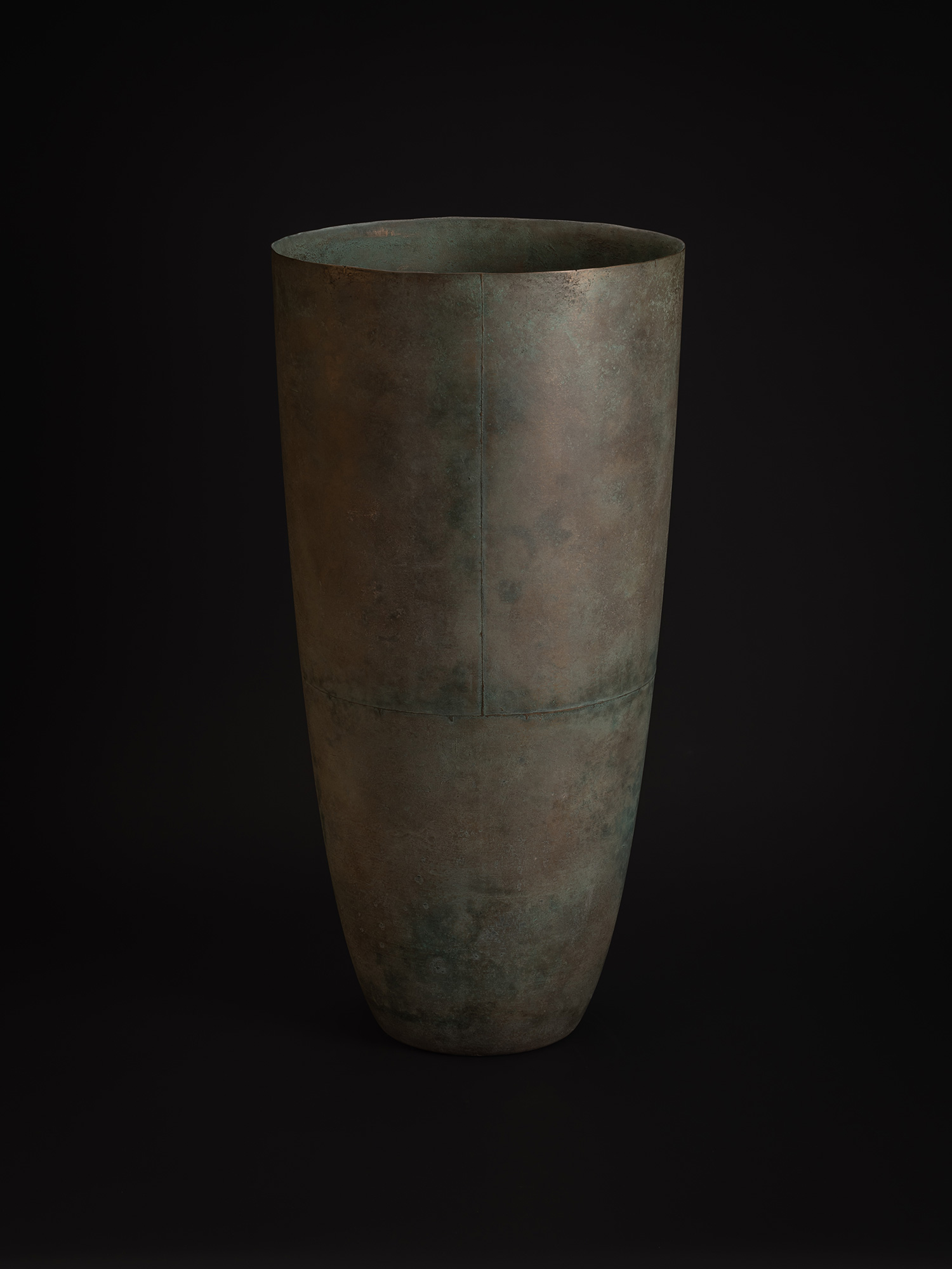 This angle highlights the vessel’s curved profile and expansive upper opening. The bronze surface...