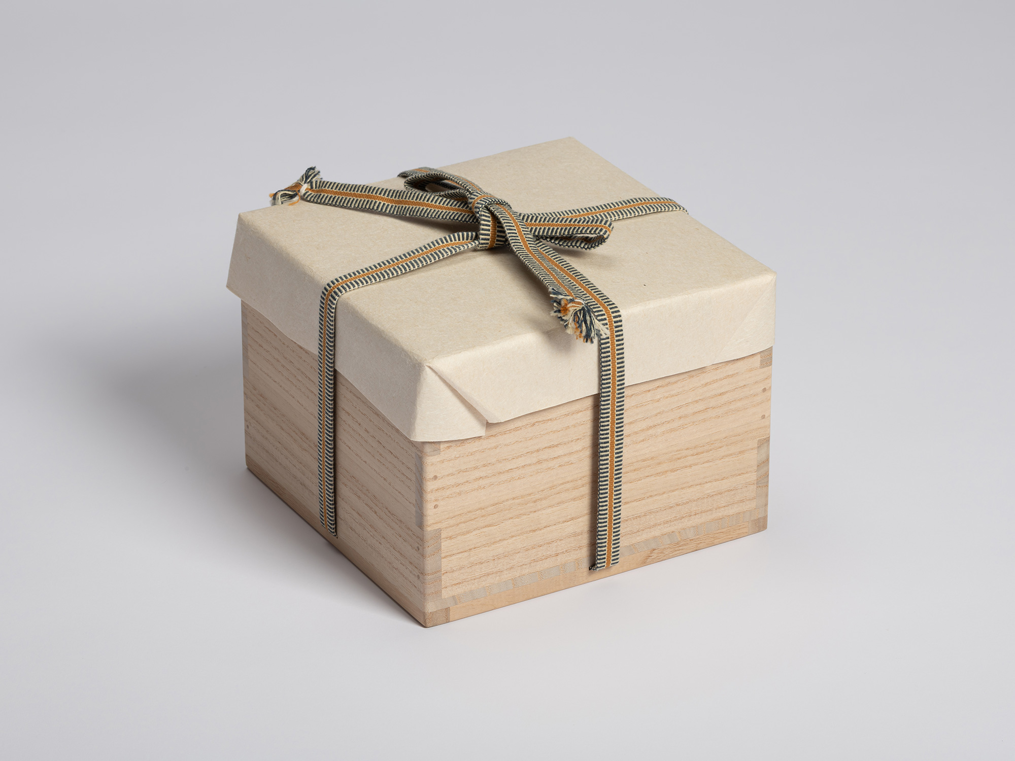 Paulownia wood tomobako wrapped in protective cream-colored paper and secured with a striped braided...