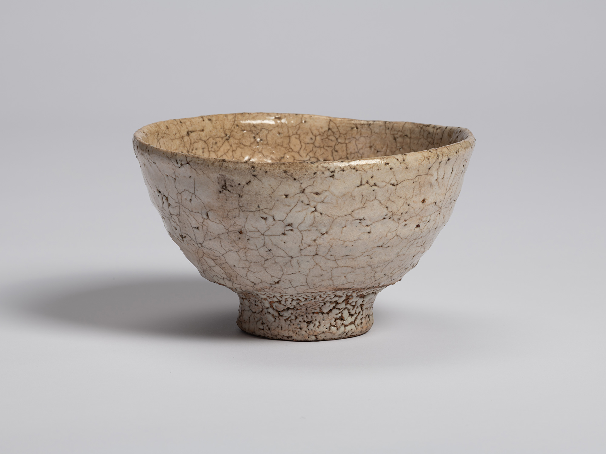 View of Ido Chawan showing its asymmetrical profile and slightly irregular rim. The pale glaze...