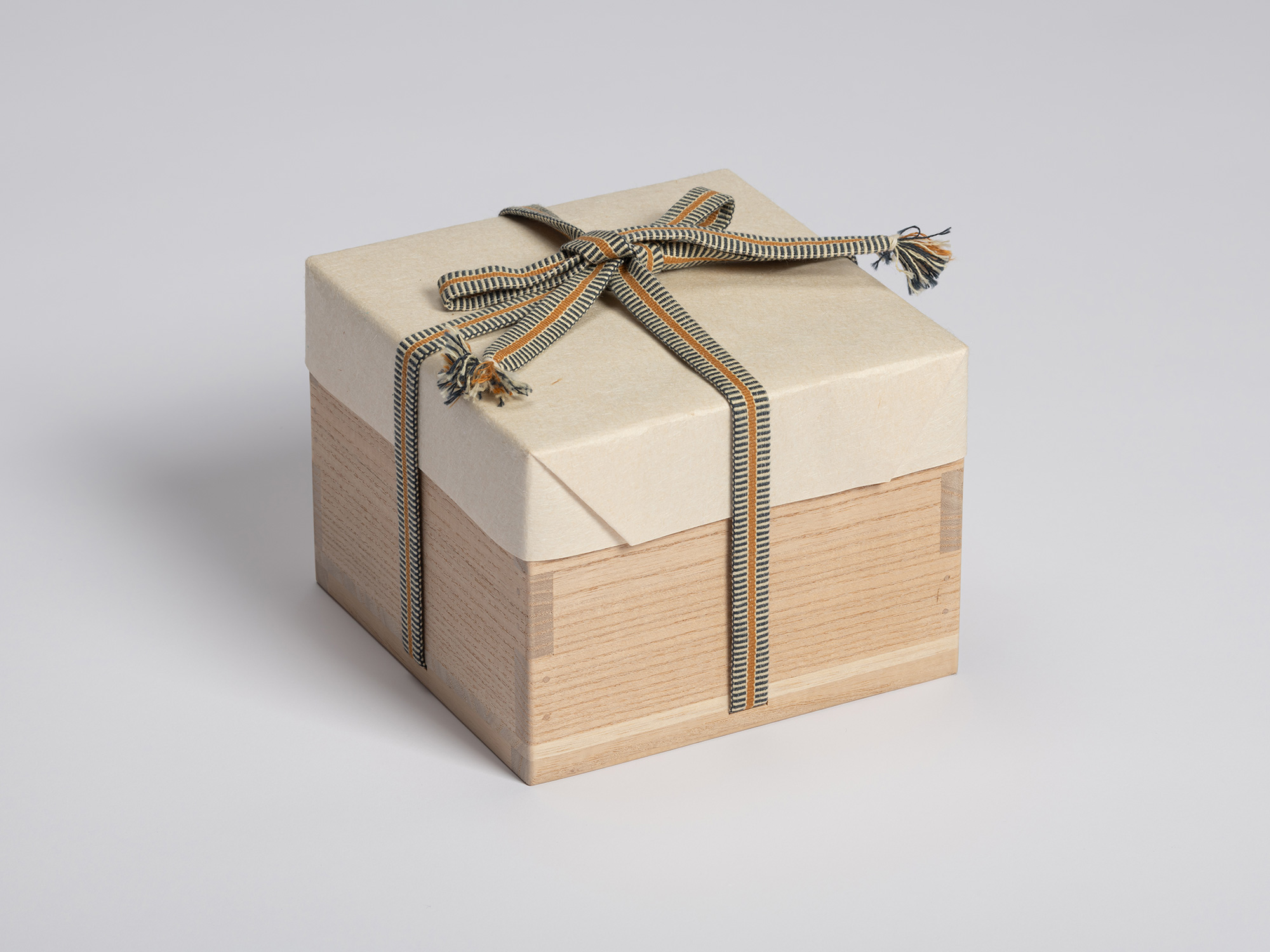 Three-quarter view of the tomobako wrapped in protective paper and secured with a striped braided...
