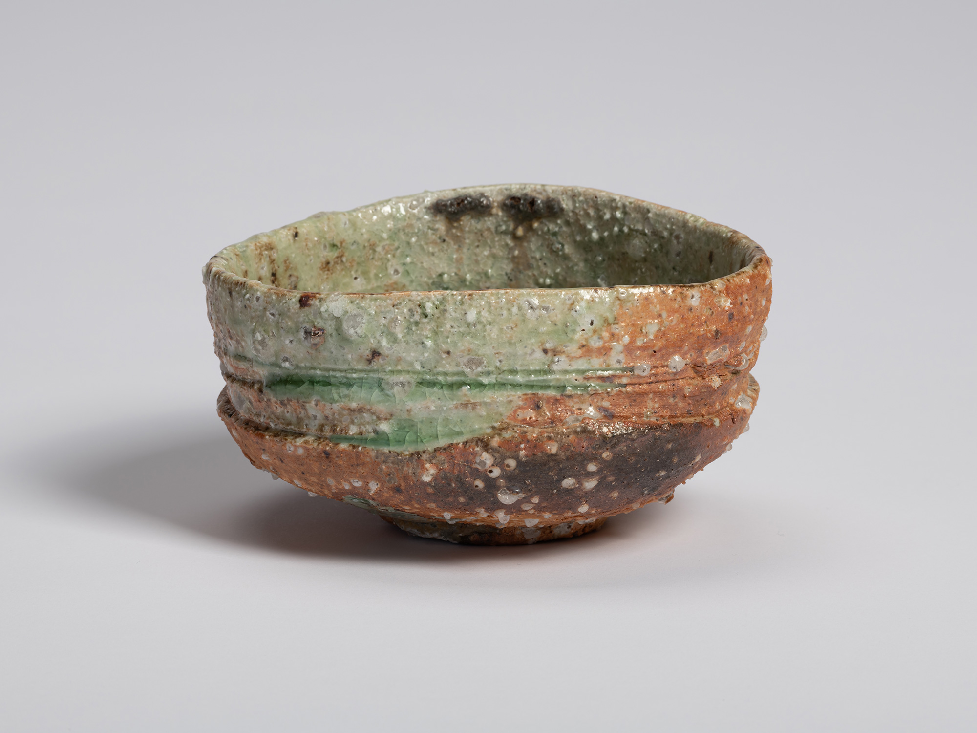 Iga tea bowl by Shiro Tsujimura photographed against a light background. The bowl features an uneven...