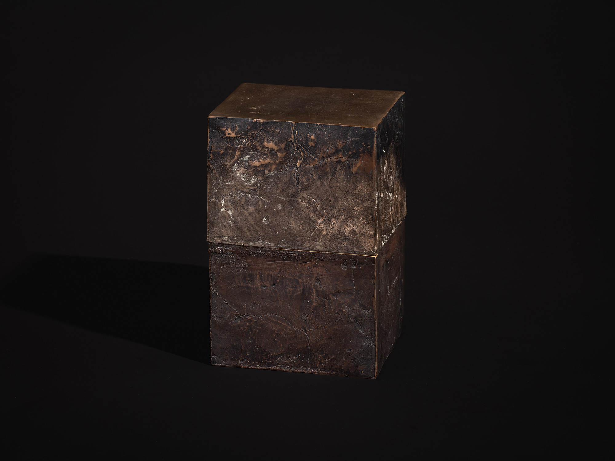 Inner Existence shown in its assembled state as a compact, vertically oriented bronze box. The...