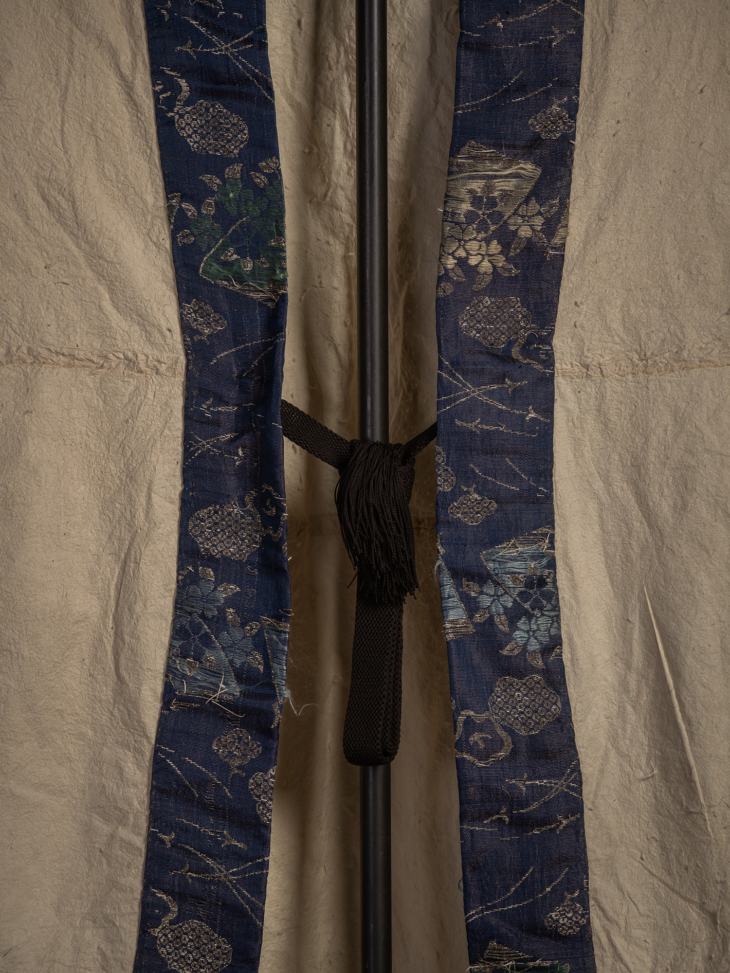 Detail view of the lower section of the blue silk collar and its black braided fastening cord with...