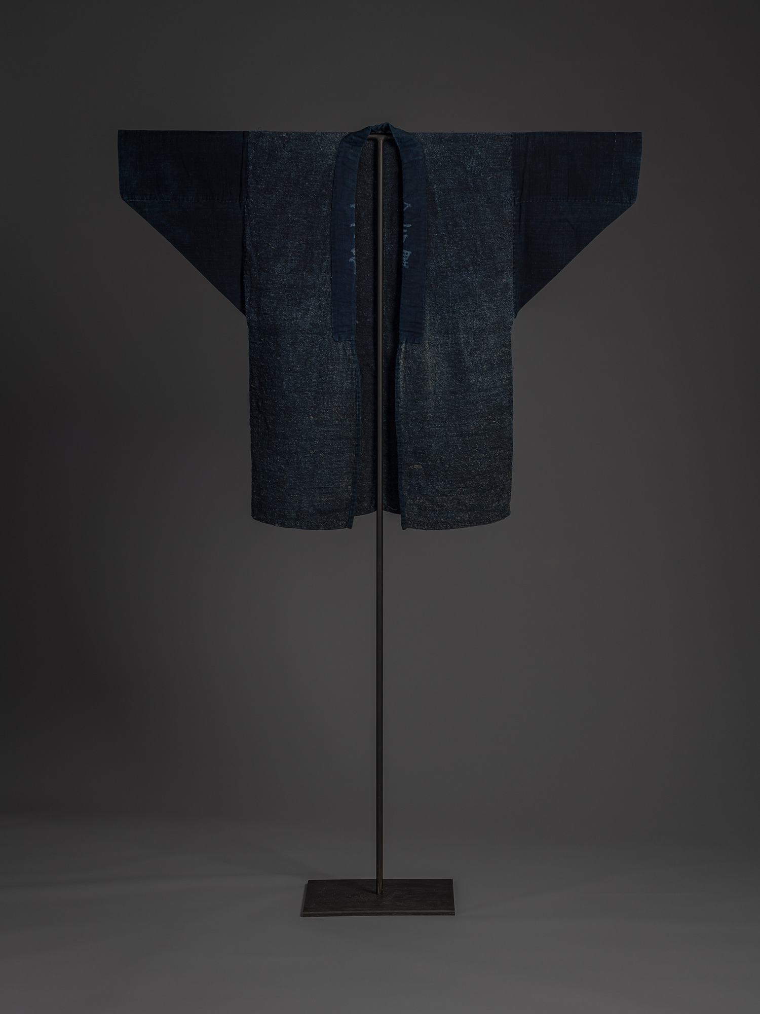 Front view of an okusozakkuri work jacket woven from coarse indigo-dyed cloth. The long indigo...