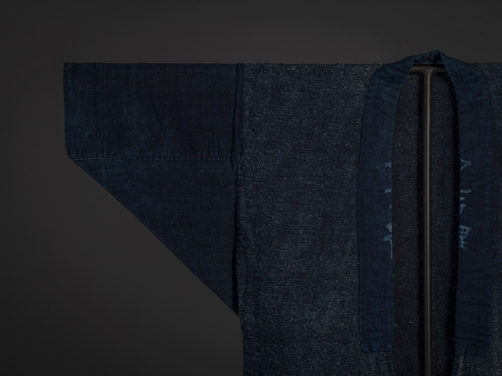 Close-up of the front collar of the indigo okusozakkuri work jacket. The long, smooth indigo cotton...
