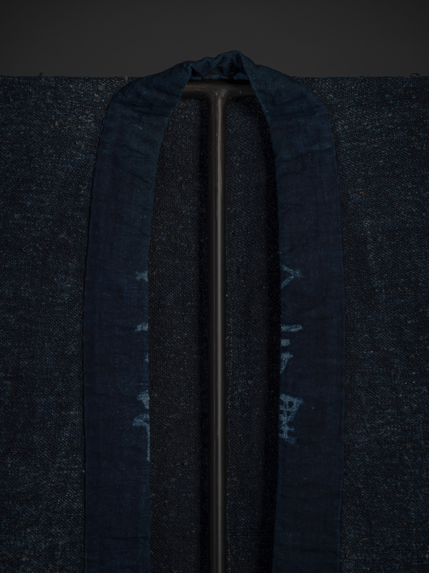 Close-up of the front left shoulder and collar of the indigo okusozakkuri. The textured handwoven...