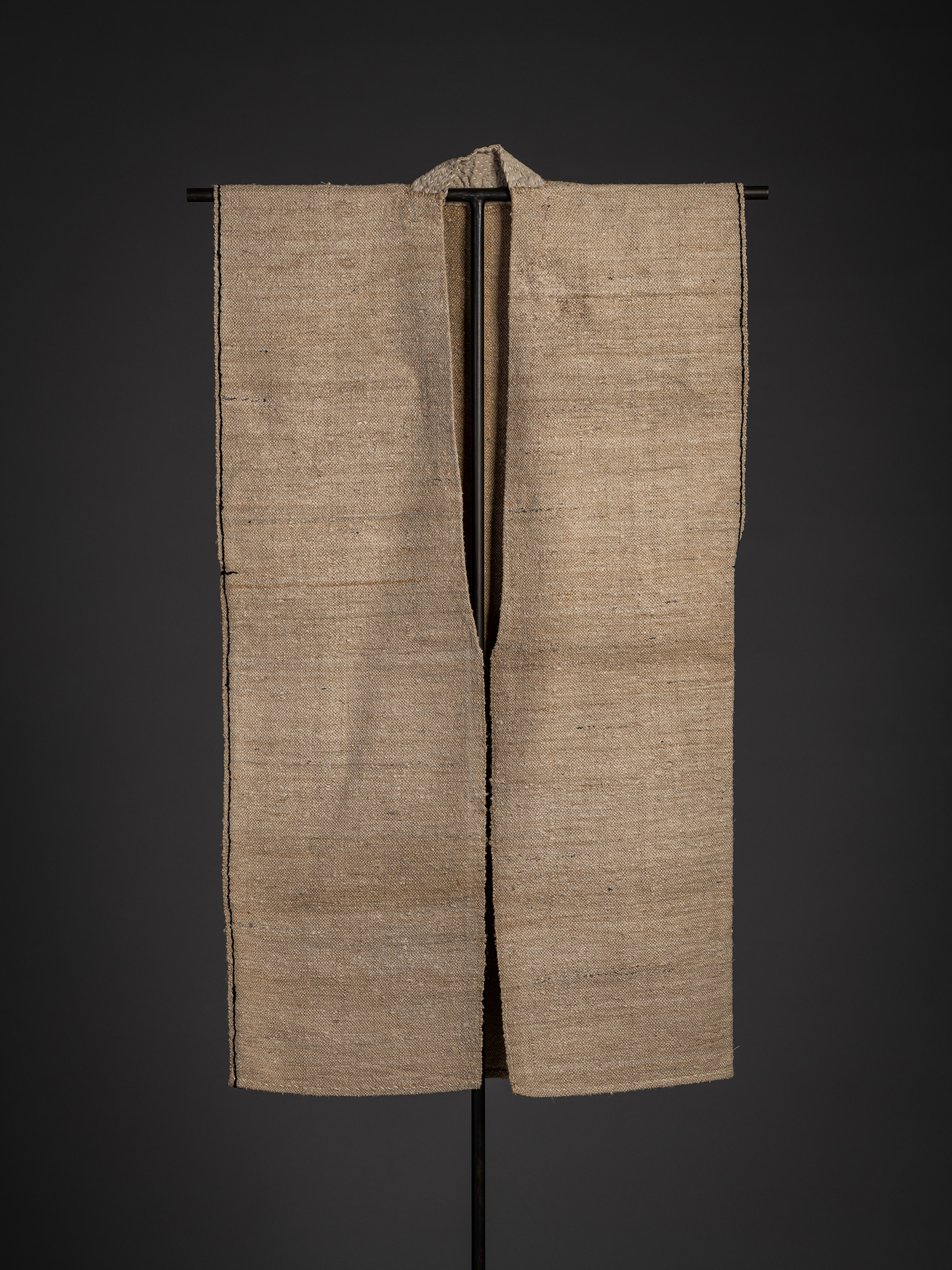 Full front view of an okusozakkuri sleeveless work garment displayed on a black stand. Constructed...