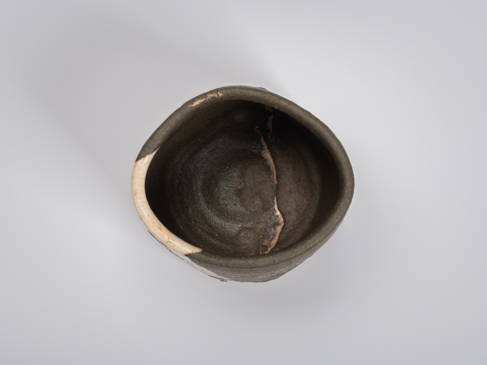 Overhead view of the tea bowl revealing its irregular circular opening and dark interior. A pale...