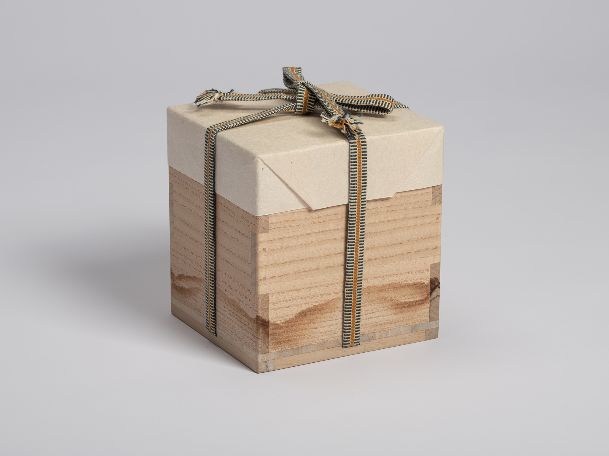 Wooden tomobako wrapped in protective paper and secured with a striped cord tied in a bow across...