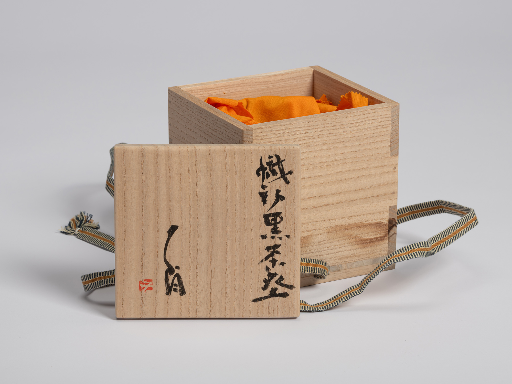 Open paulownia wood tomobako for an Oribe Guro tea bowl by Shiro Tsujimura. The lid rests in front...