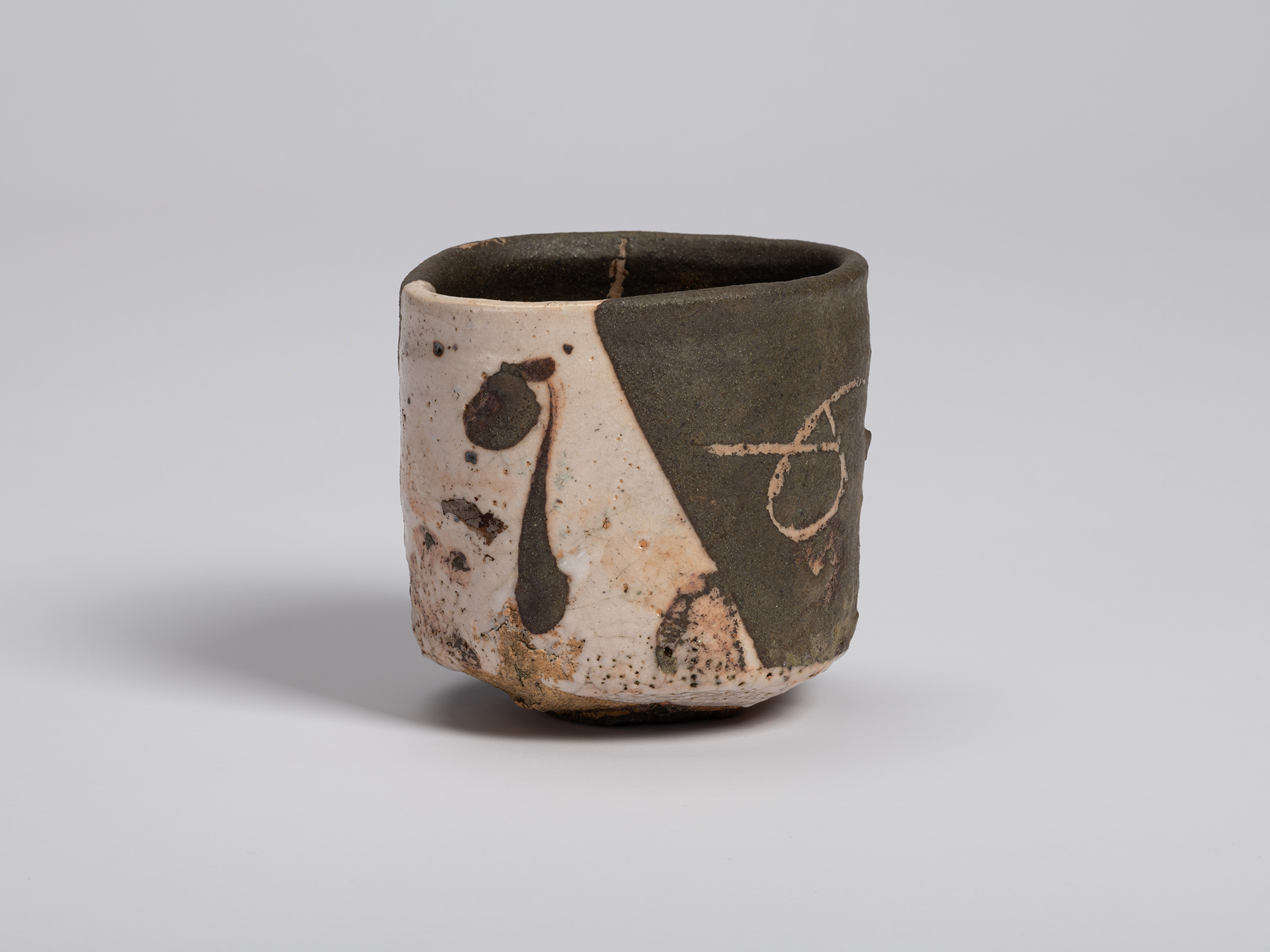 Front view of the tea bowl showing a diagonal division between white glaze and dark olive-black...