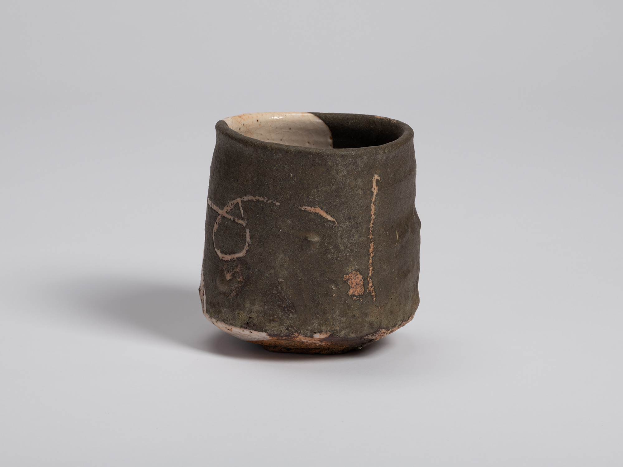 Three-quarter view highlighting the dark glazed side of the bowl. Pale incised lines loop across...