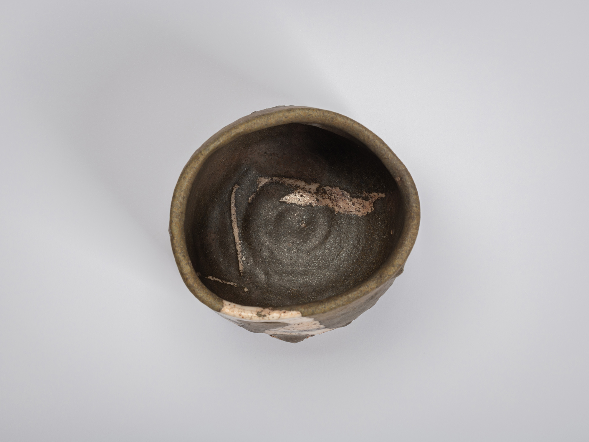 Top-down view of the Oribe Guro Chawan revealing its dark interior and irregular opening. Pale...