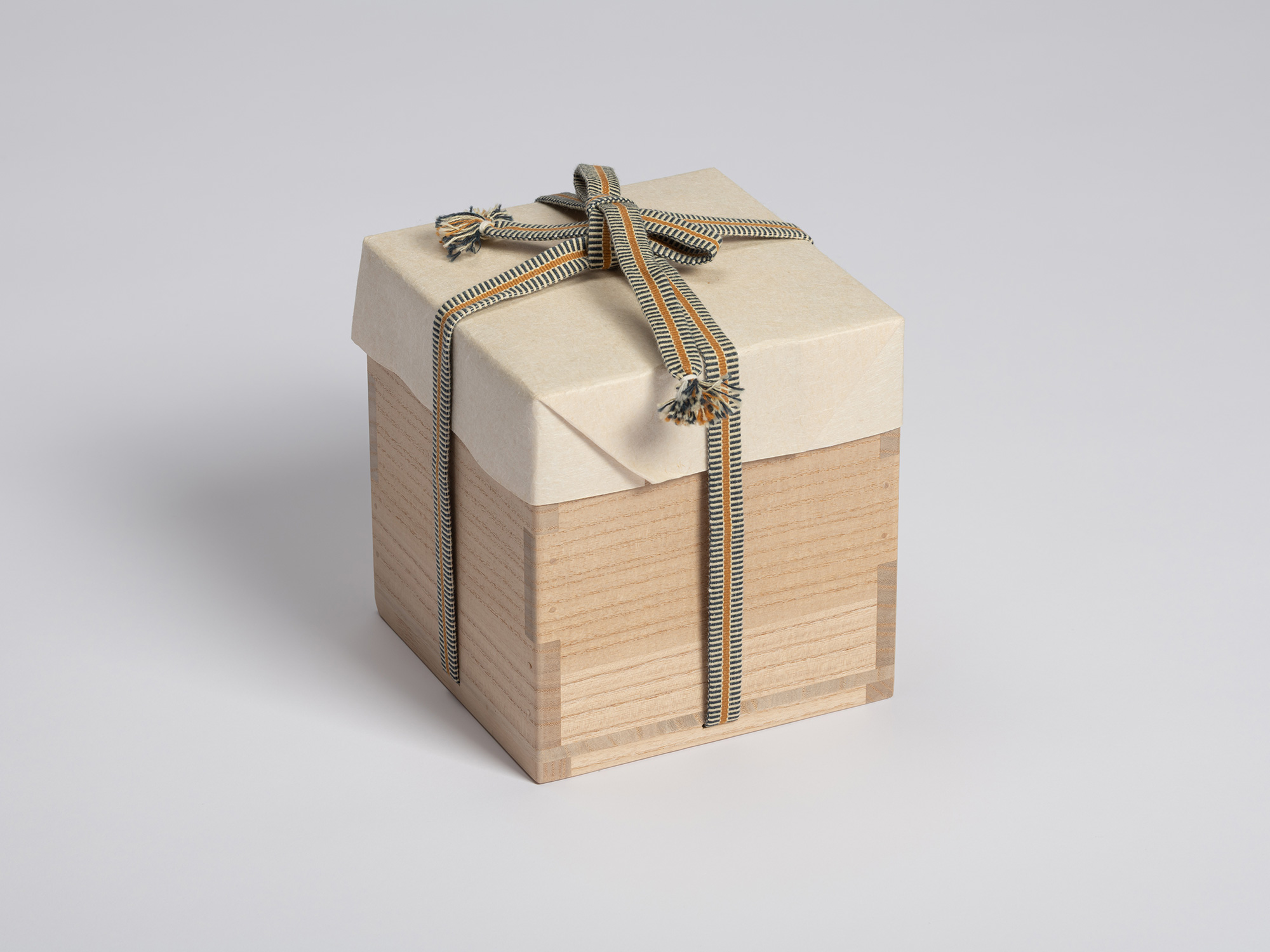 Wooden tomobako for an Oribe Guro Chawan, shown closed and wrapped in protective paper. A striped...