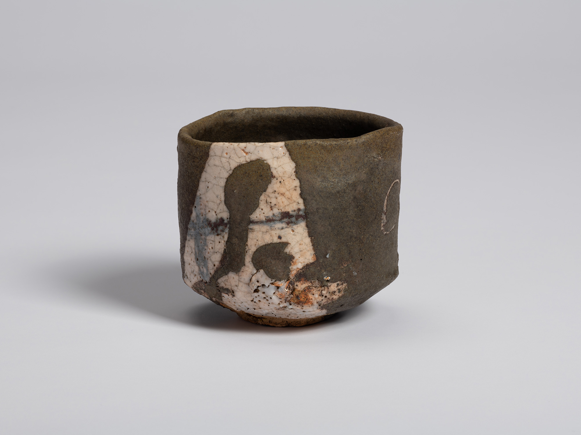 Front view of an Oribe Guro tea bowl with a dark, matte surface and an irregular cylindrical form....