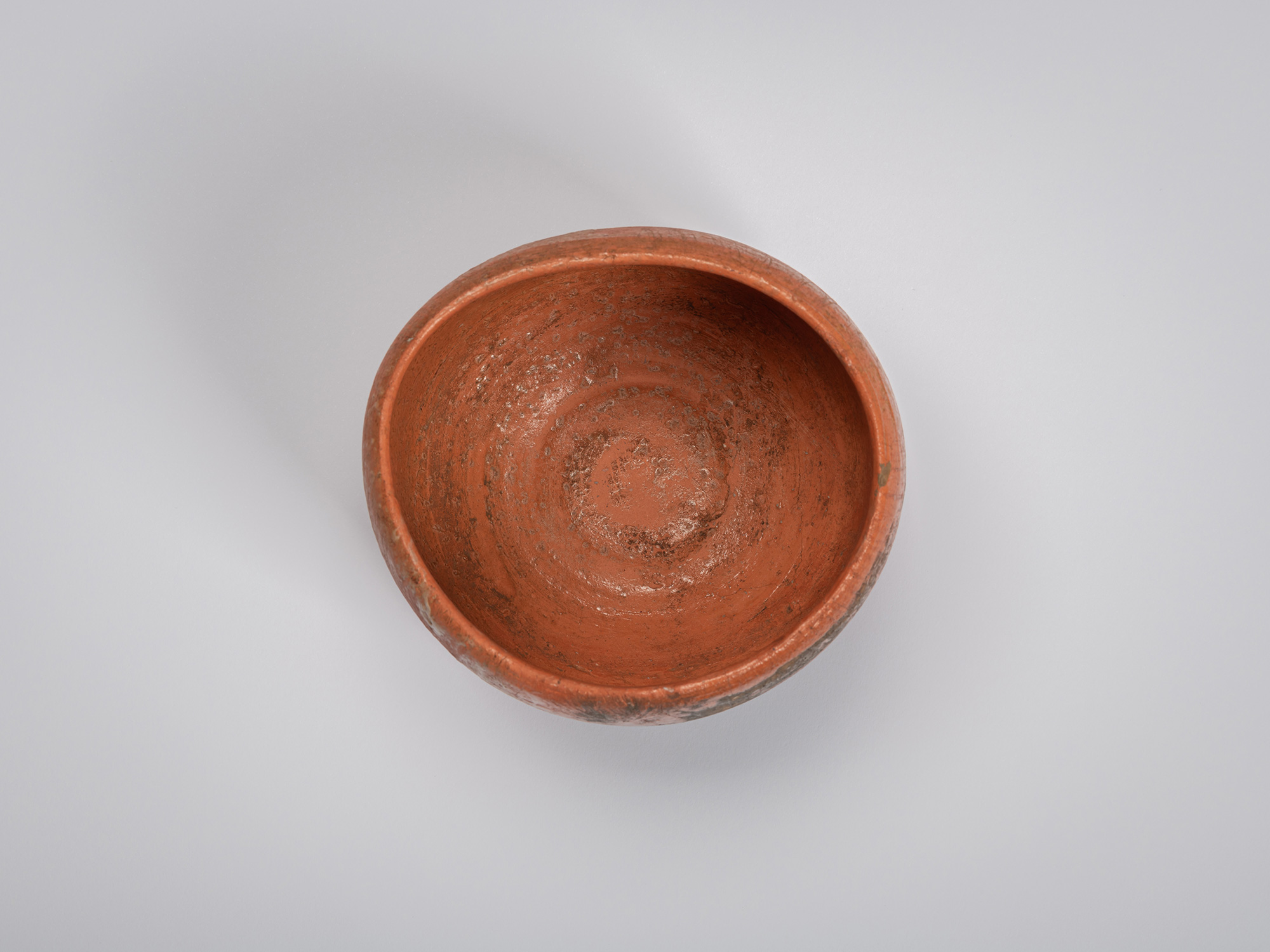 Overhead view of a red Raku tea bowl by Shiro Tsujimura. The interior is finished in the same warm...