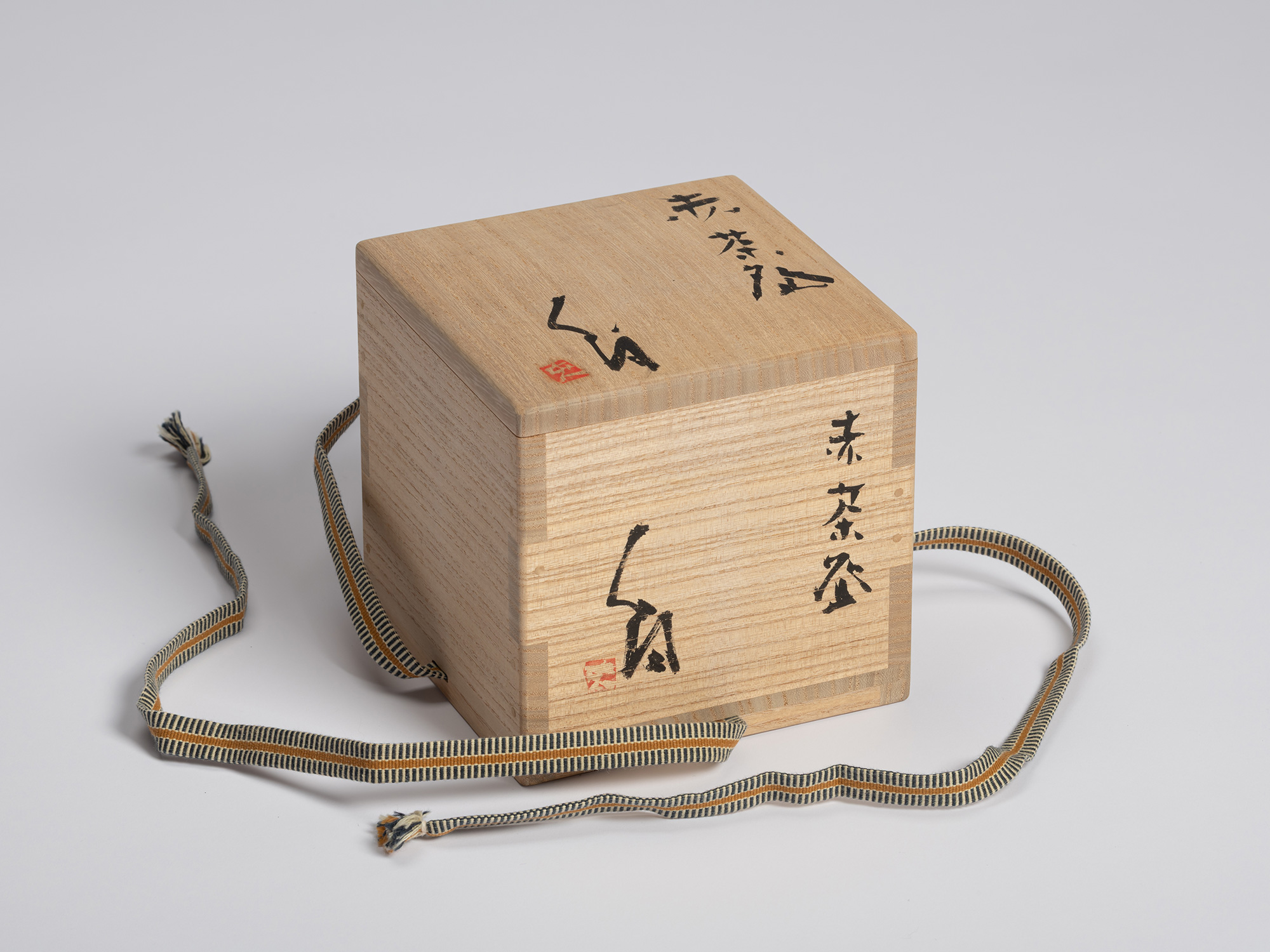 A light-colored wooden paulownia storage box (kiribako) for a Japanese tea bowl, shown fully closed...