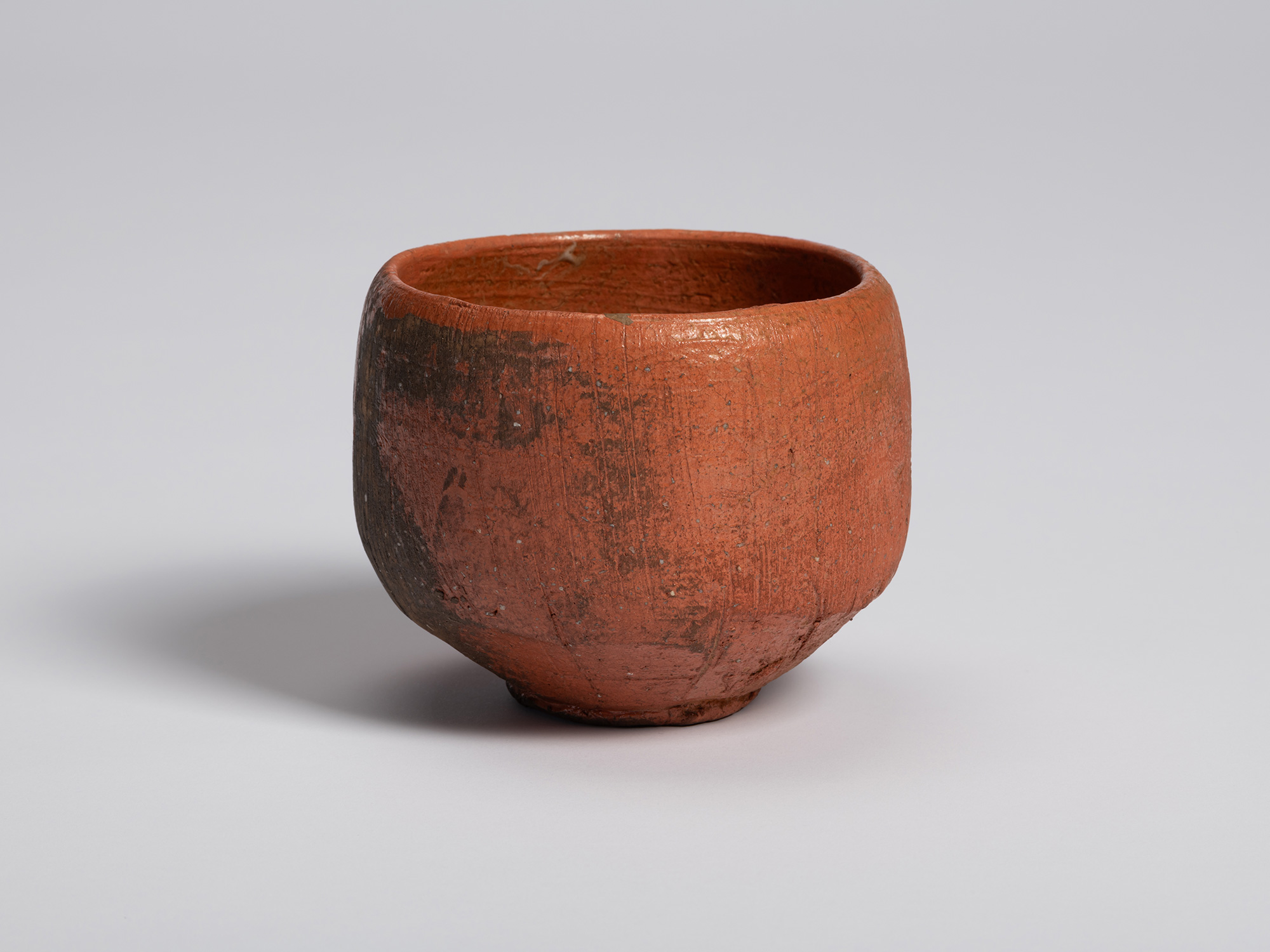 Red Raku tea bowl by Shiro Tsujimura. The rounded form narrows toward the foot, while a dark firing...