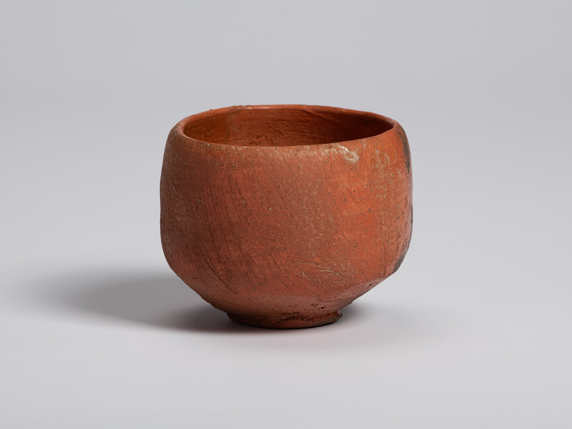 Red Raku tea bowl by Shiro Tsujimura with a rounded, hand-formed silhouette and softly flared rim....