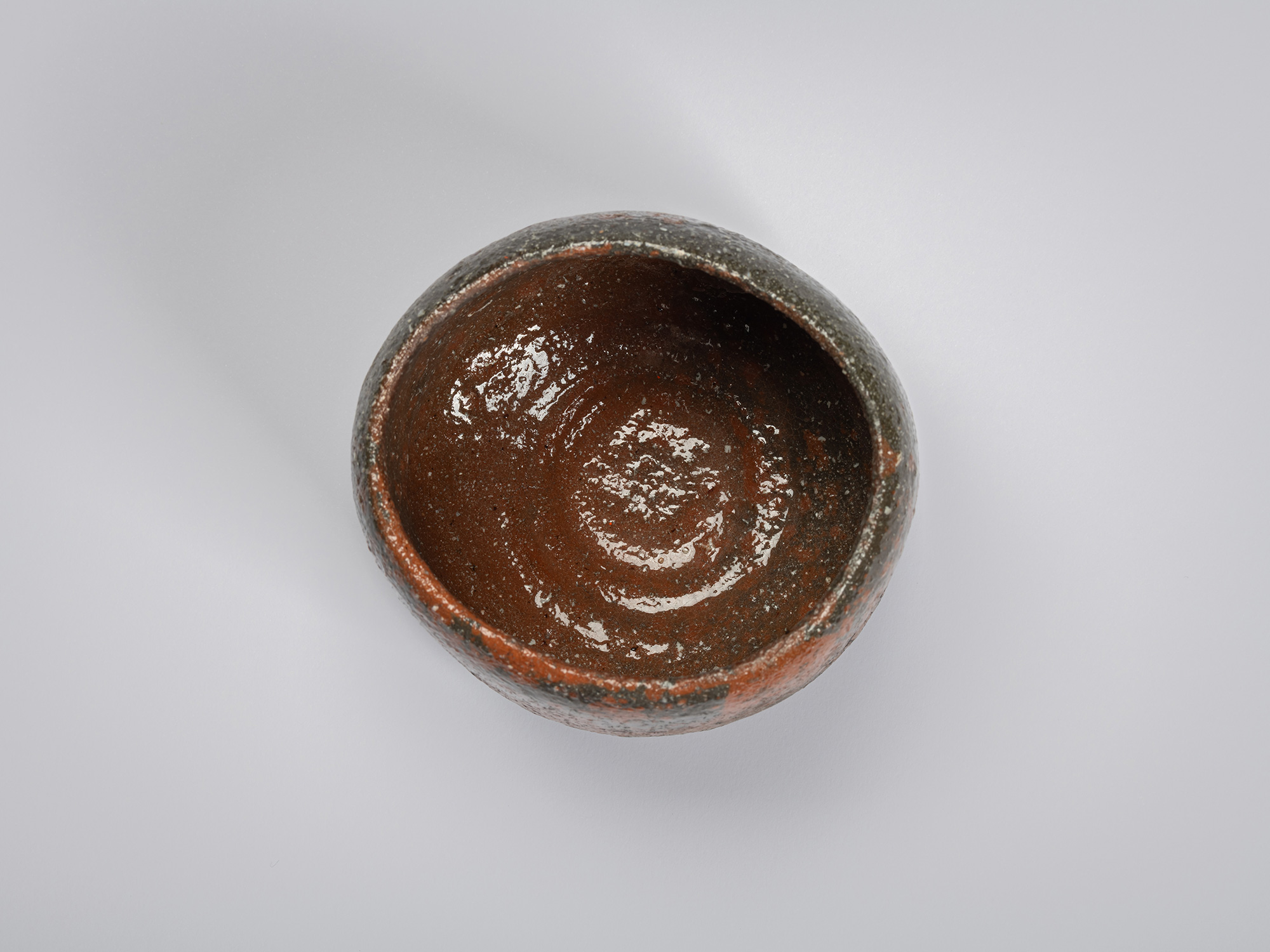 Overhead view looking into Shiro Tsujimura’s raku-style tea bowl. The interior has a glossy, dark...