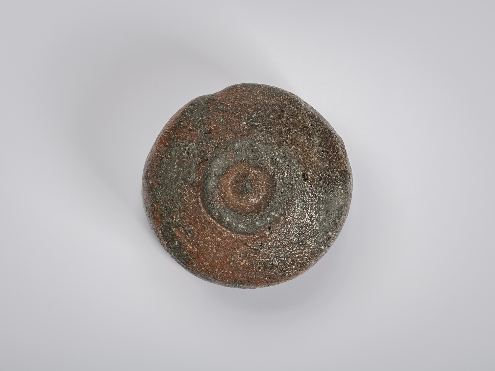 Underside view of a raku-style tea bowl by Shiro Tsujimura. The rounded base reveals a small circular...