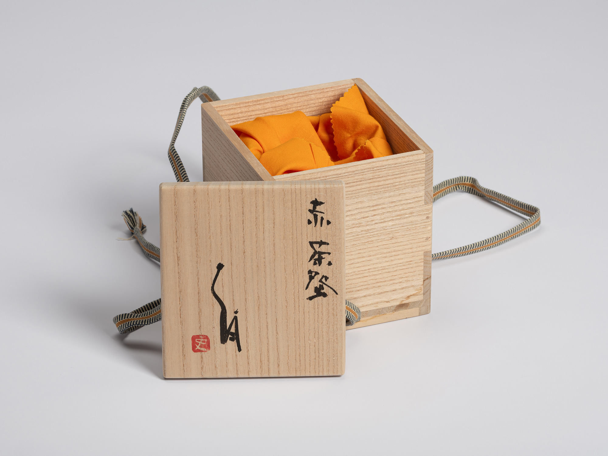 Open kiri wood tomobako for Shiro Tsujimura’s red raku tea bowl. The lid is placed in front of...