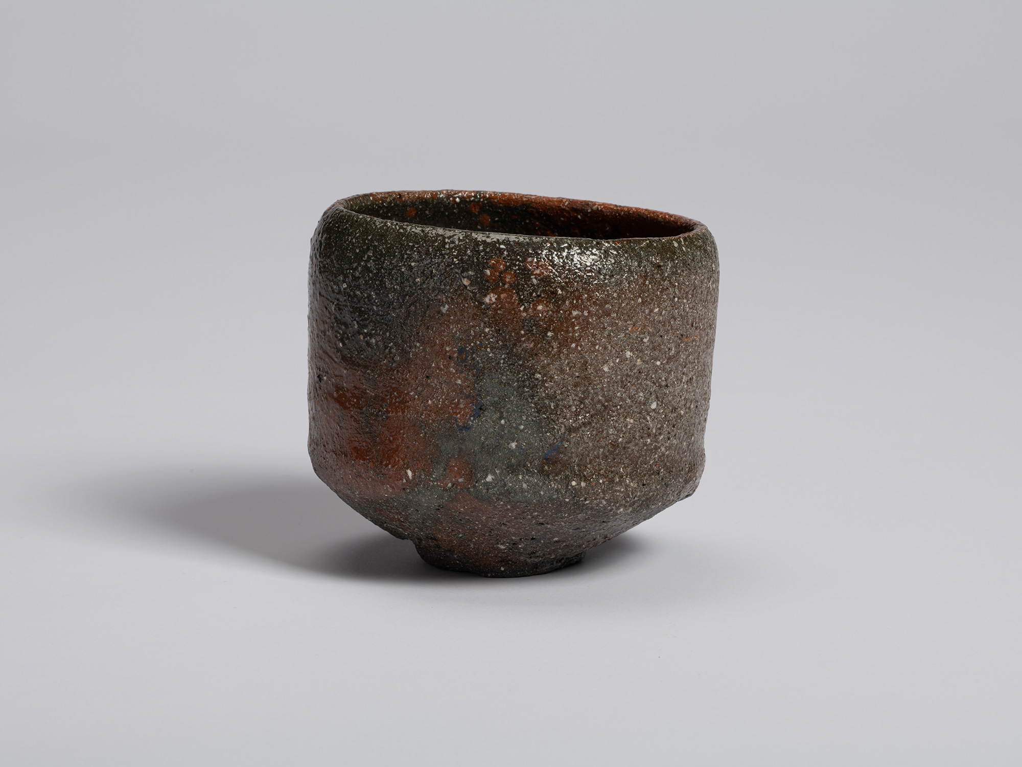 View of a raku-style tea bowl showing a transition from iron-red clay tones to darker charcoal...