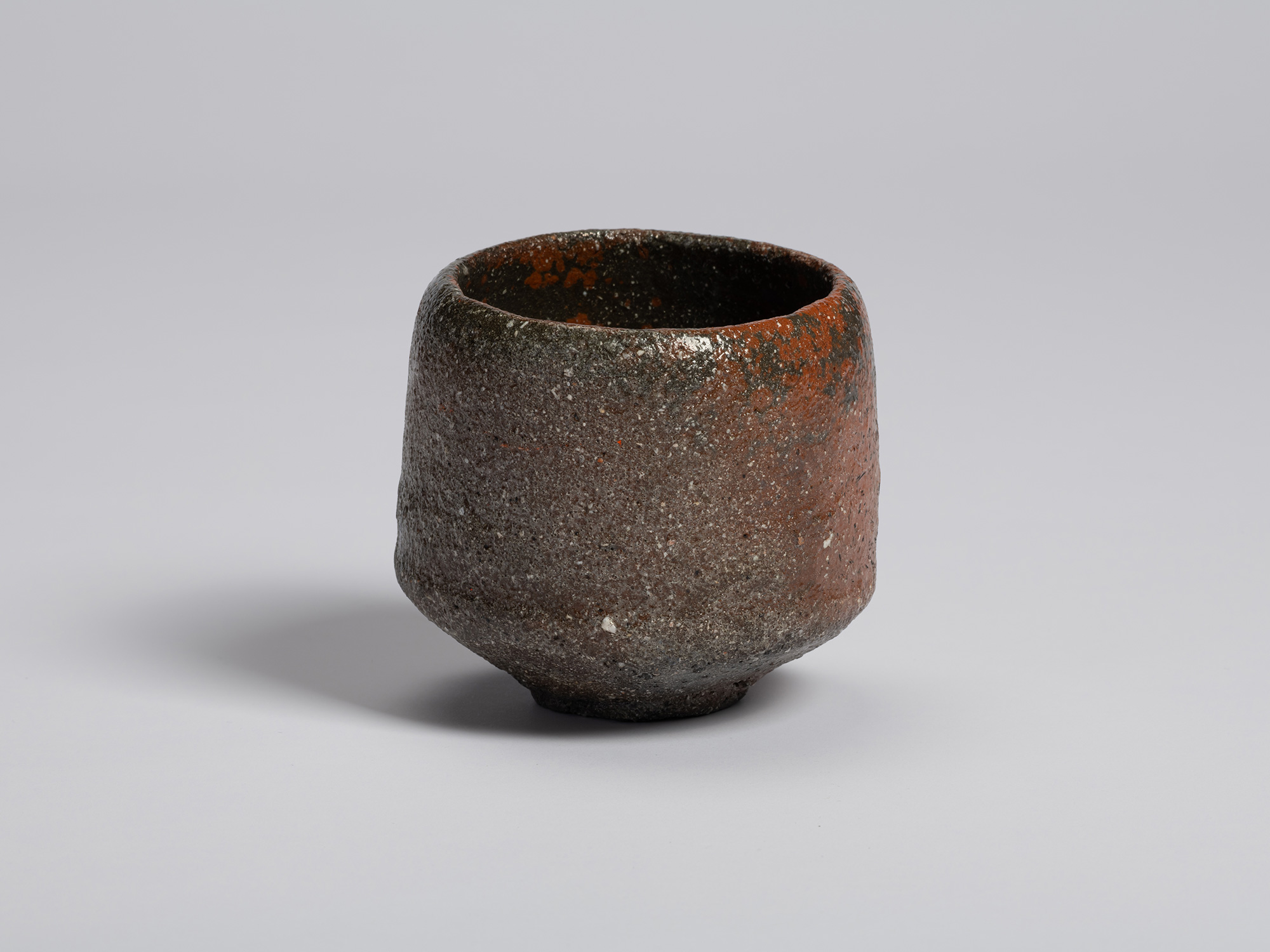 View of Shiro Tsujimura’s raku-style tea bowl. The surface is predominantly dark gray with areas...