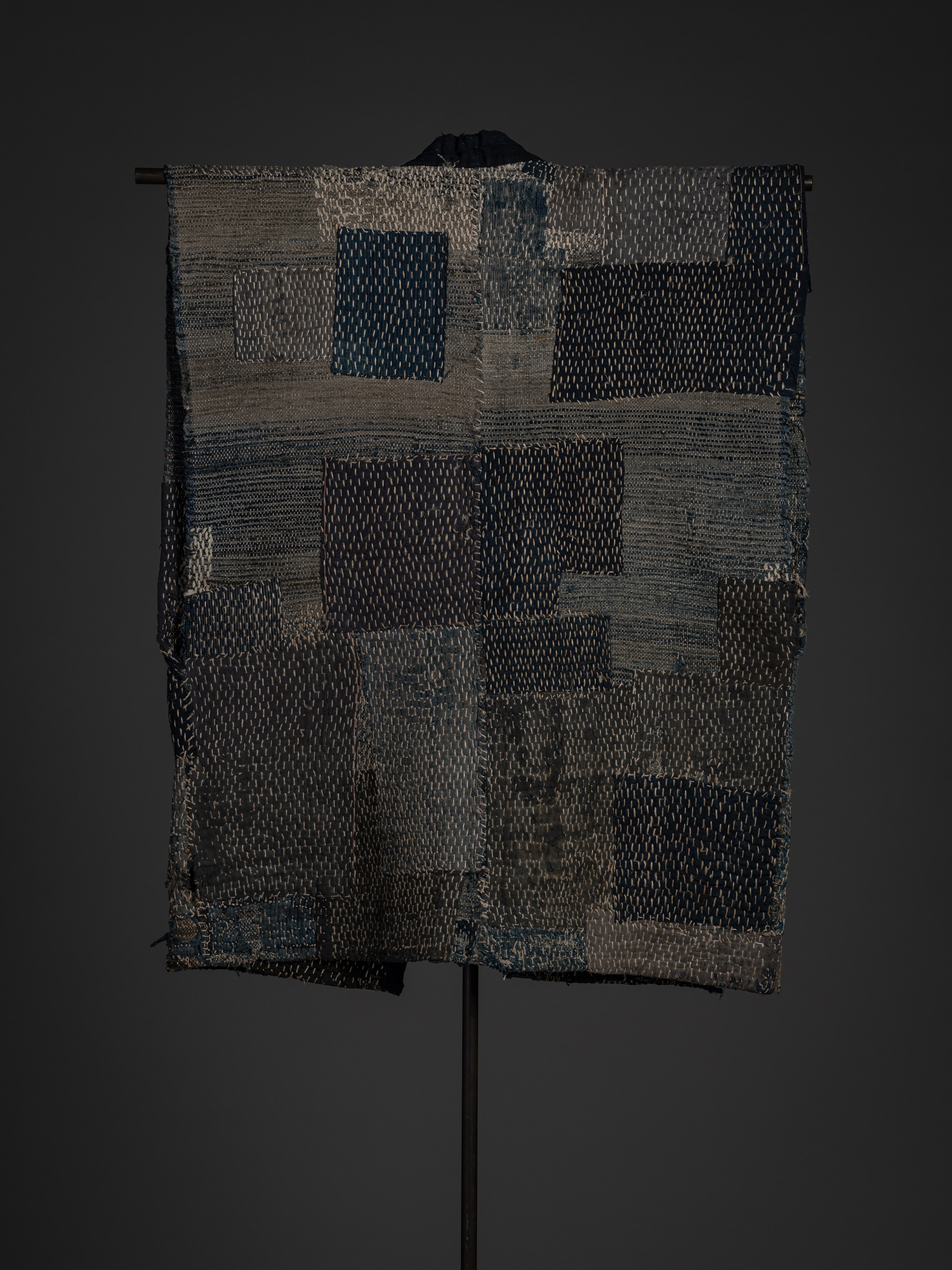Full back view of a Japanese sakiori boro work coat made of cotton and hemp. The back is composed...
