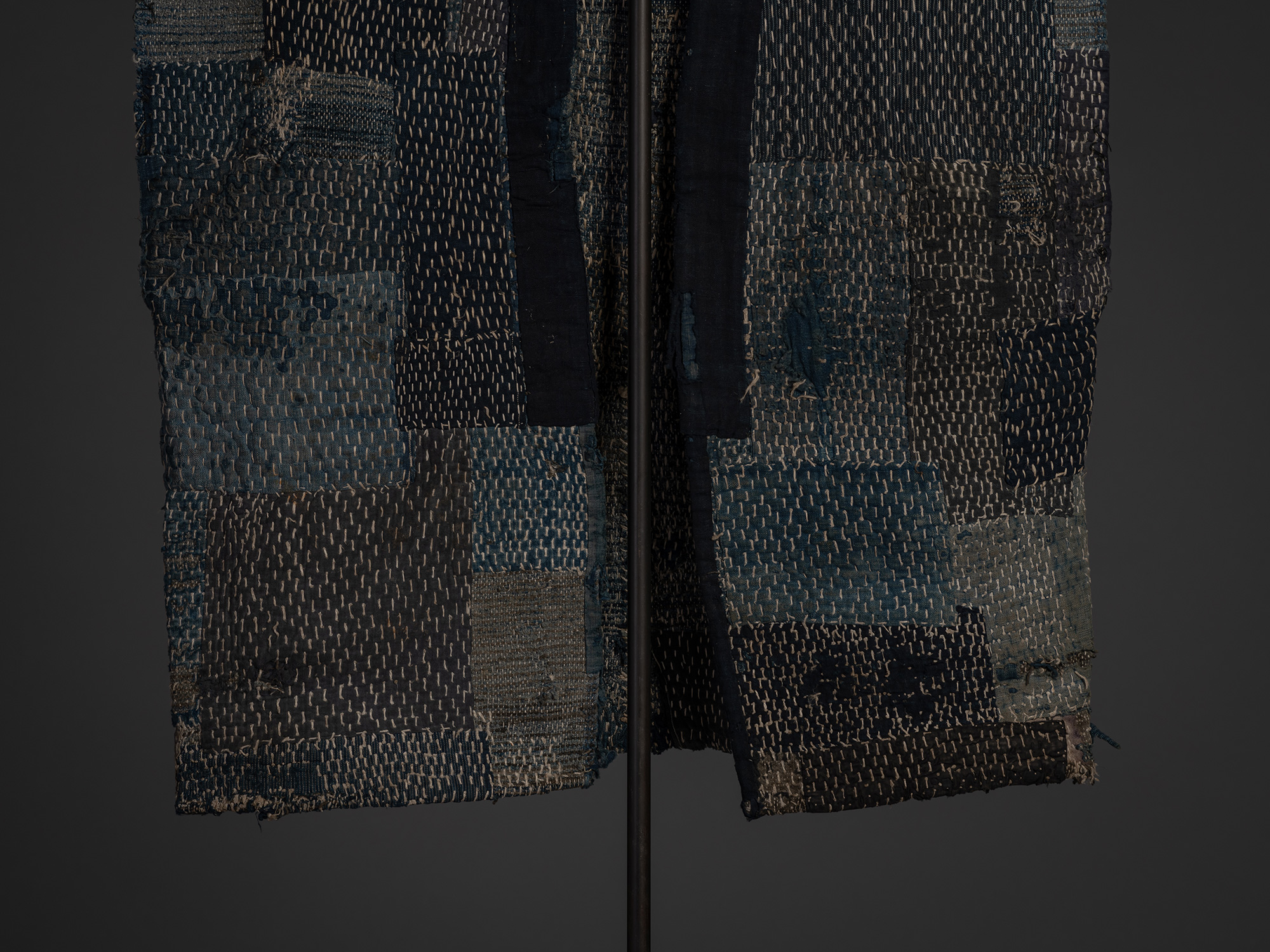 Close-up of the lower front of the sakiori boro work coat with the long dark indigo collar hanging...