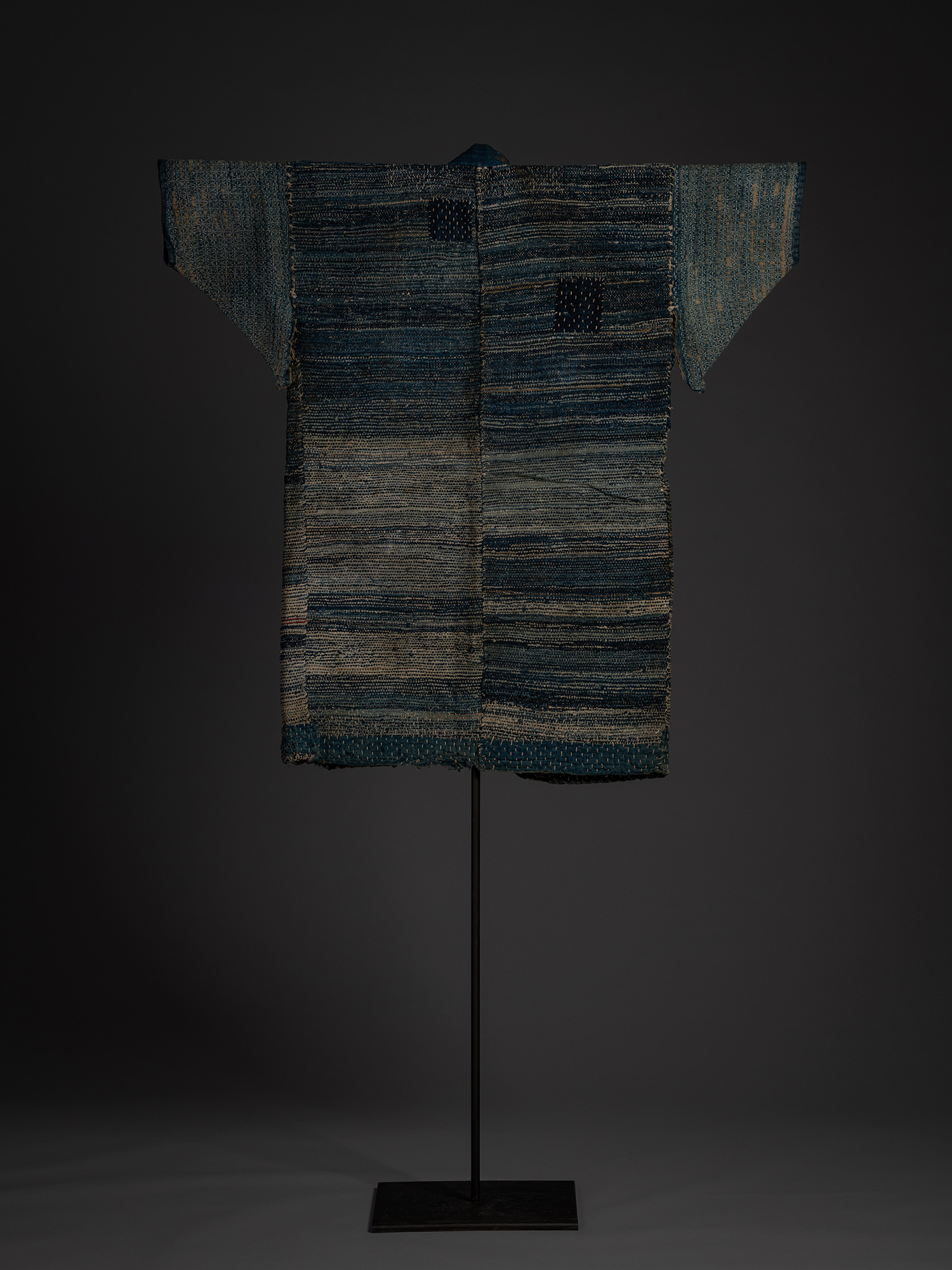 Back view of a Japanese sakiori hanten made from indigo-dyed cotton and hemp, displayed on a stand....