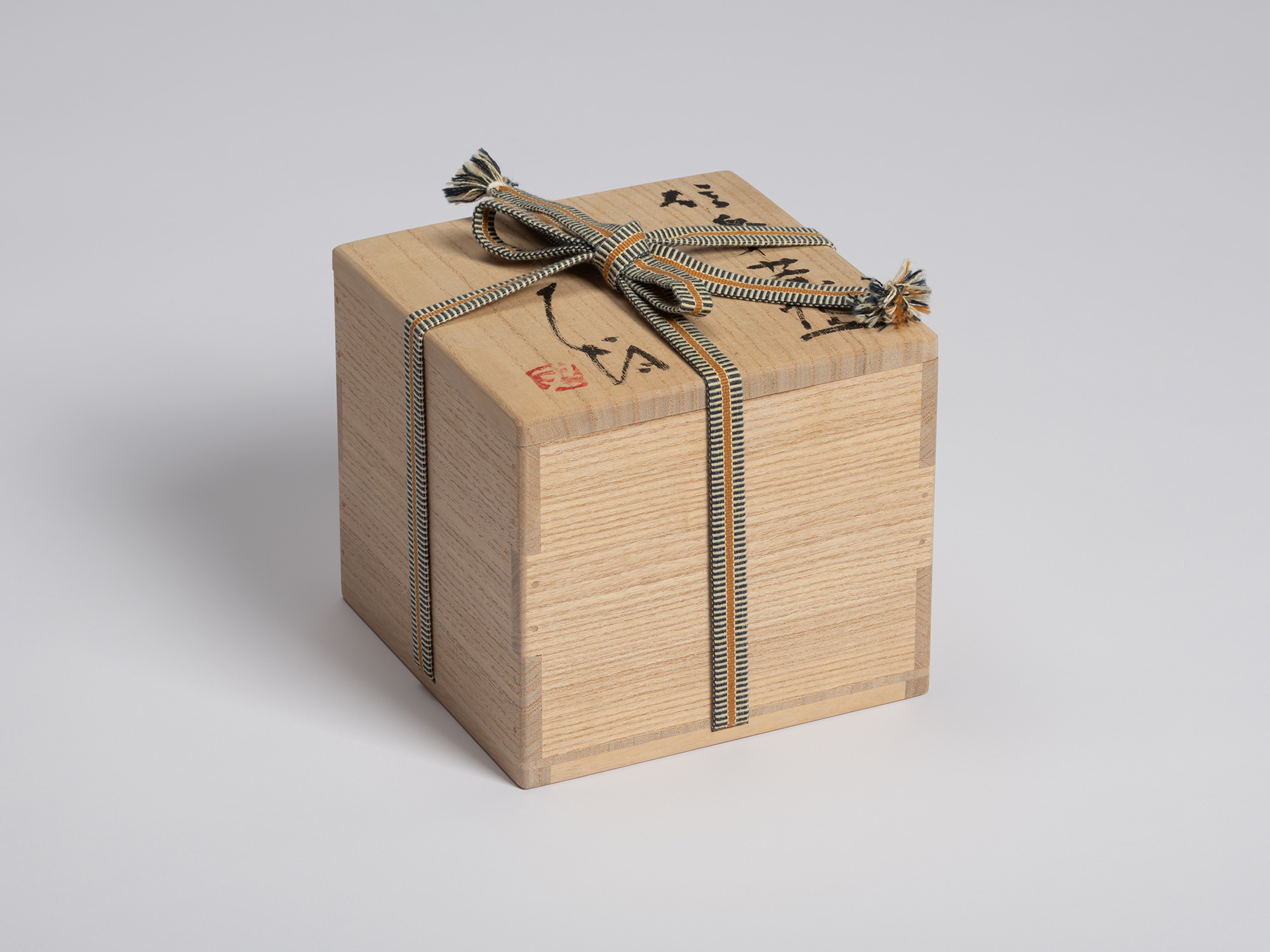 Closed wooden tomobako for Shigaraki Tsu Tsu Chawan, tied with a blue, cream, and tan striped cord....
