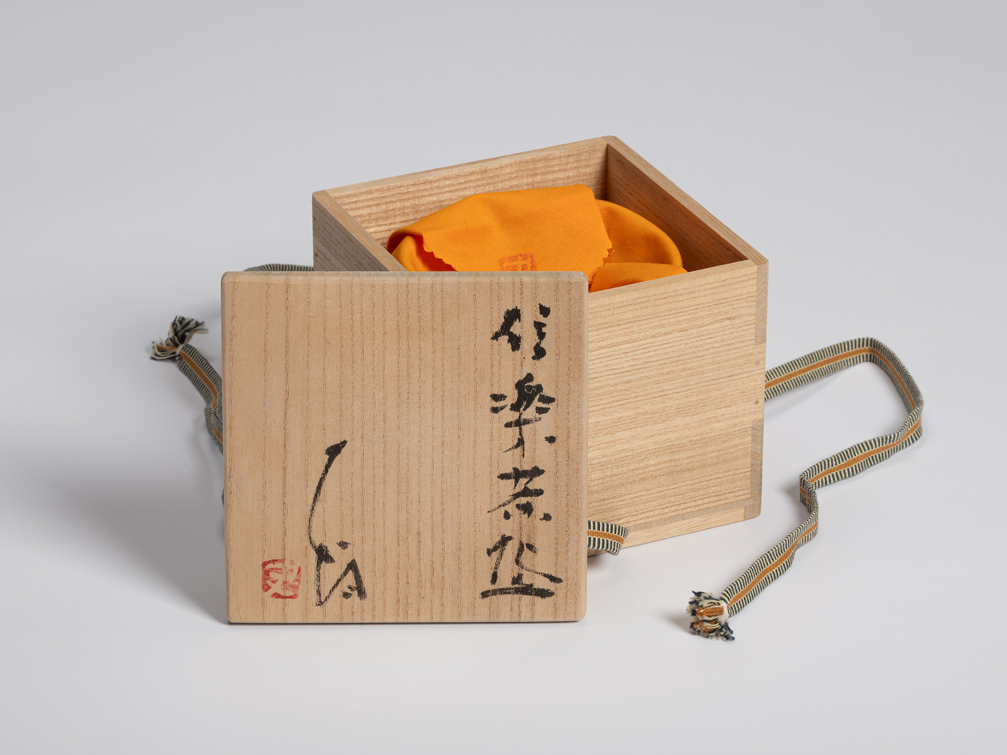 Wooden tomobako displayed with the lid leaning against the open box. Black calligraphy on the lid...