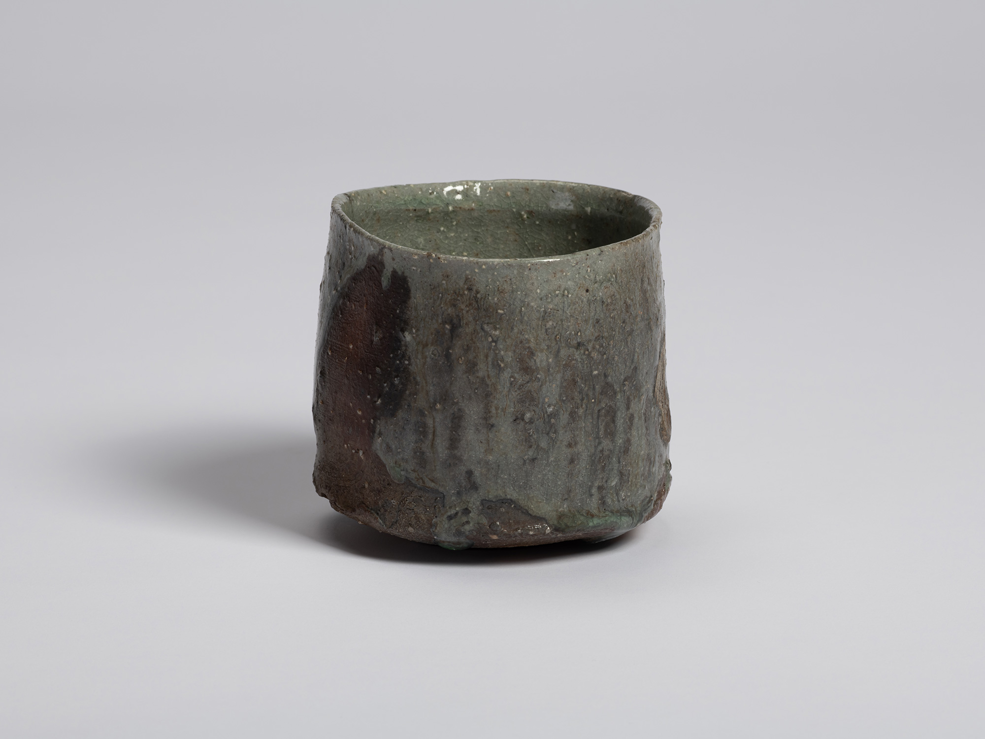 Three-quarter view of the tea bowl showing its slightly irregular cylindrical form. Green-gray...