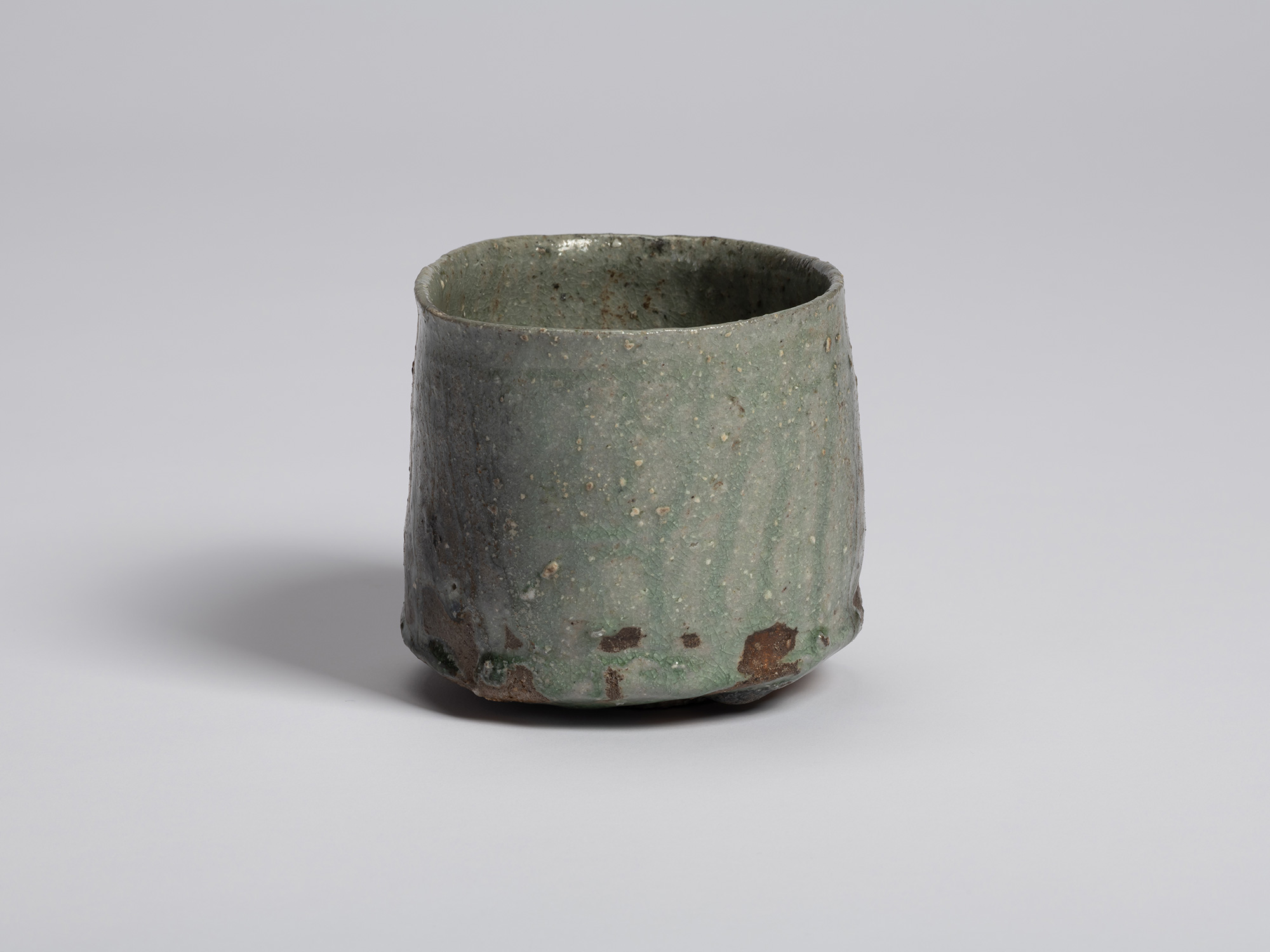 Side view of the bowl showing a broad expanse of pale green glaze with scattered pinholing and...