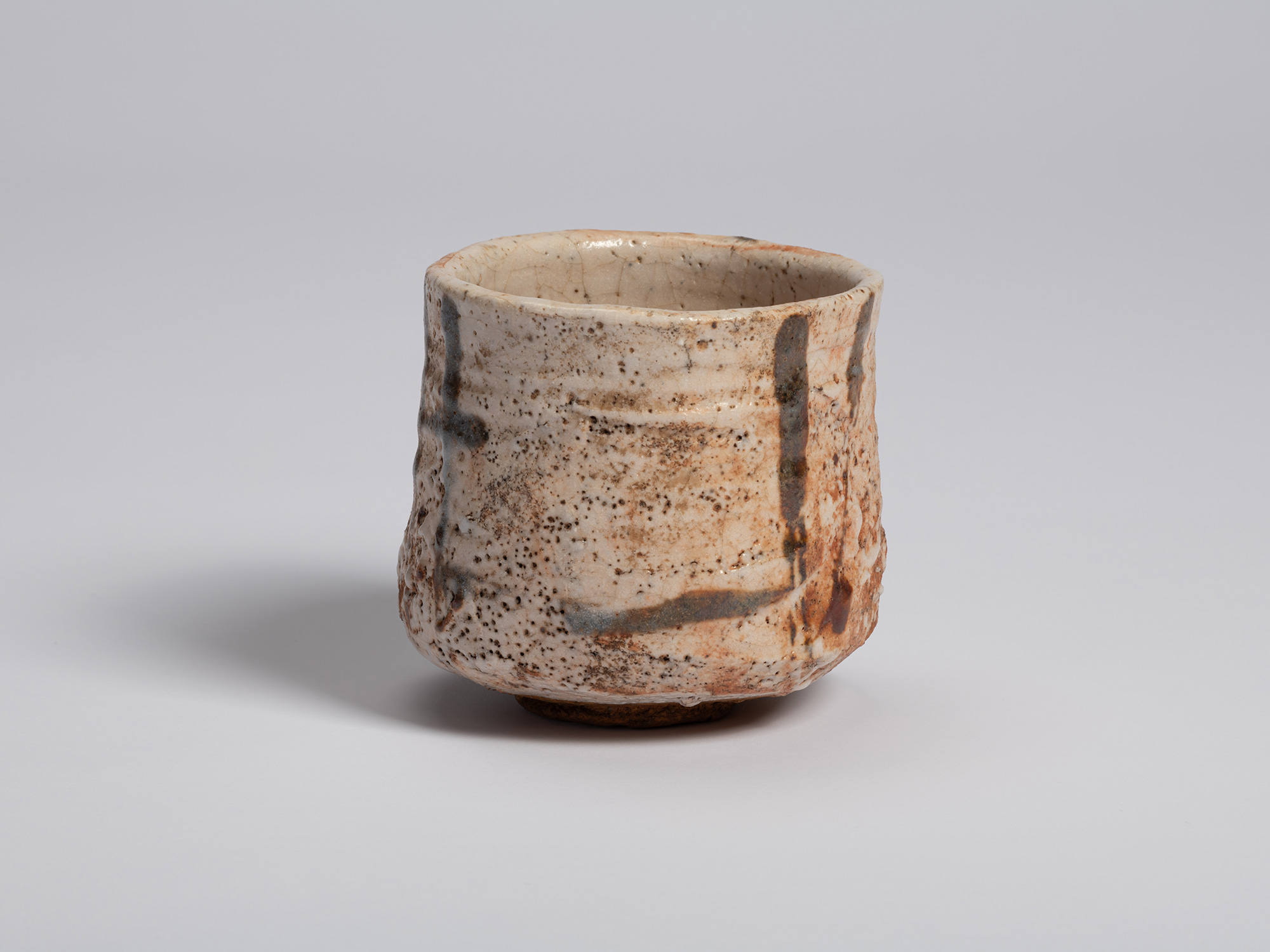 View of a Shino Chawan showing its slightly irregular, hand-formed profile. Gray brushwork lines,...