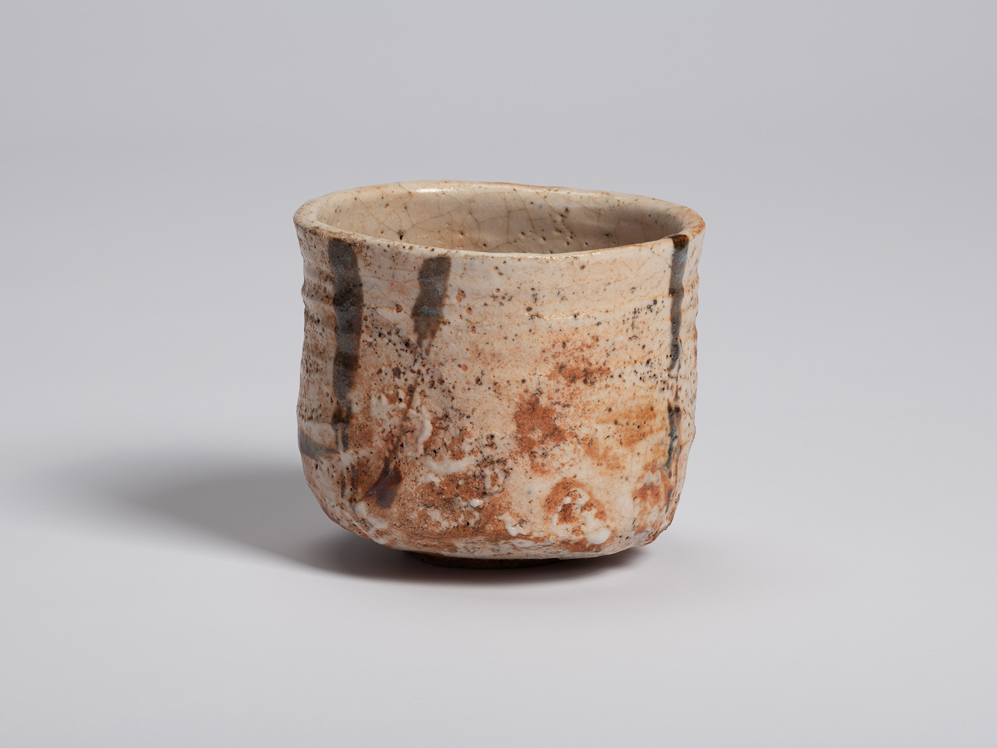 View of a Shino Chawan. Vertical gray brushstrokes descend across a field of white glaze mottled...