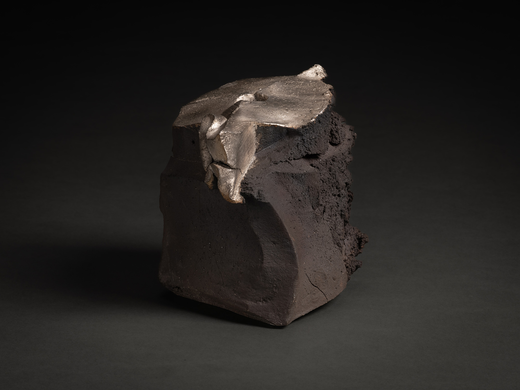 View showing the sculpture's irregular silhouette. The silver surface cascades over the upper edge,...