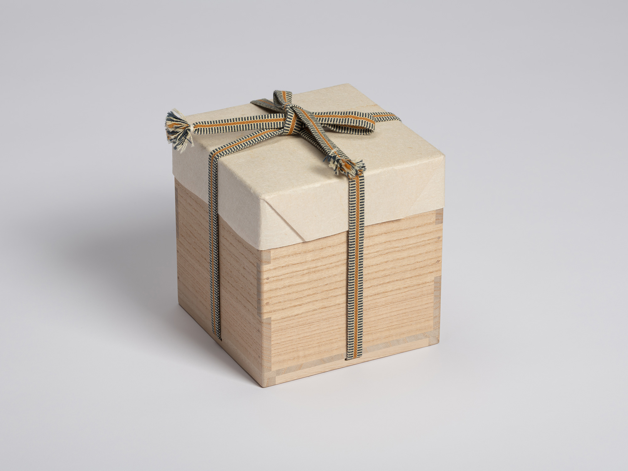 Tomobako enclosed in a cream-colored protective paper cover and secured with a striped braided...