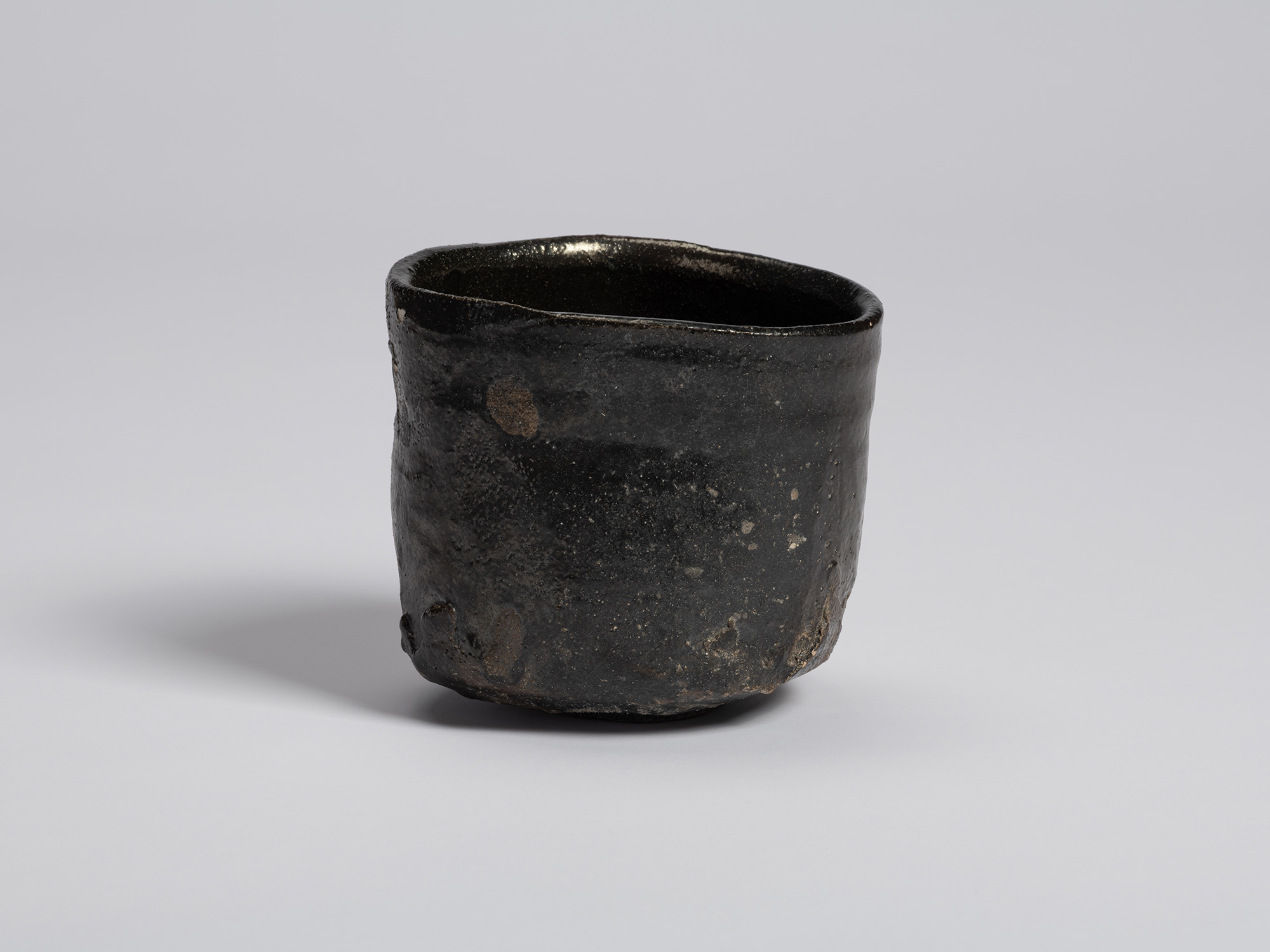 Hikidashi-type tea bowl by Shiro Tsujimura. The dark, lustrous surface shows scattered pale speckling...