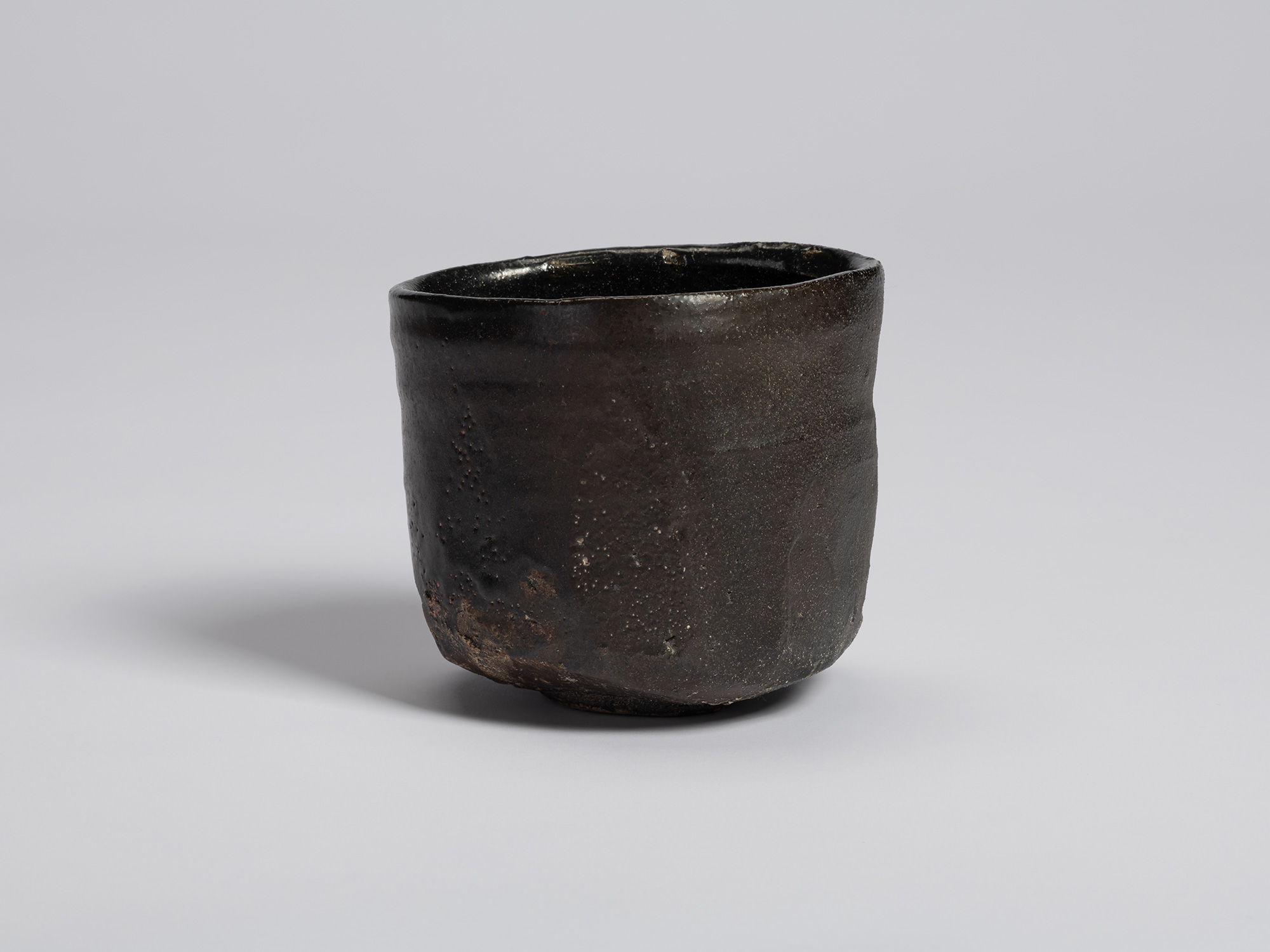 View of a hikidashi-type tea bowl by Shiro Tsujimura. The dark surface reveals fine pitting, scattered...