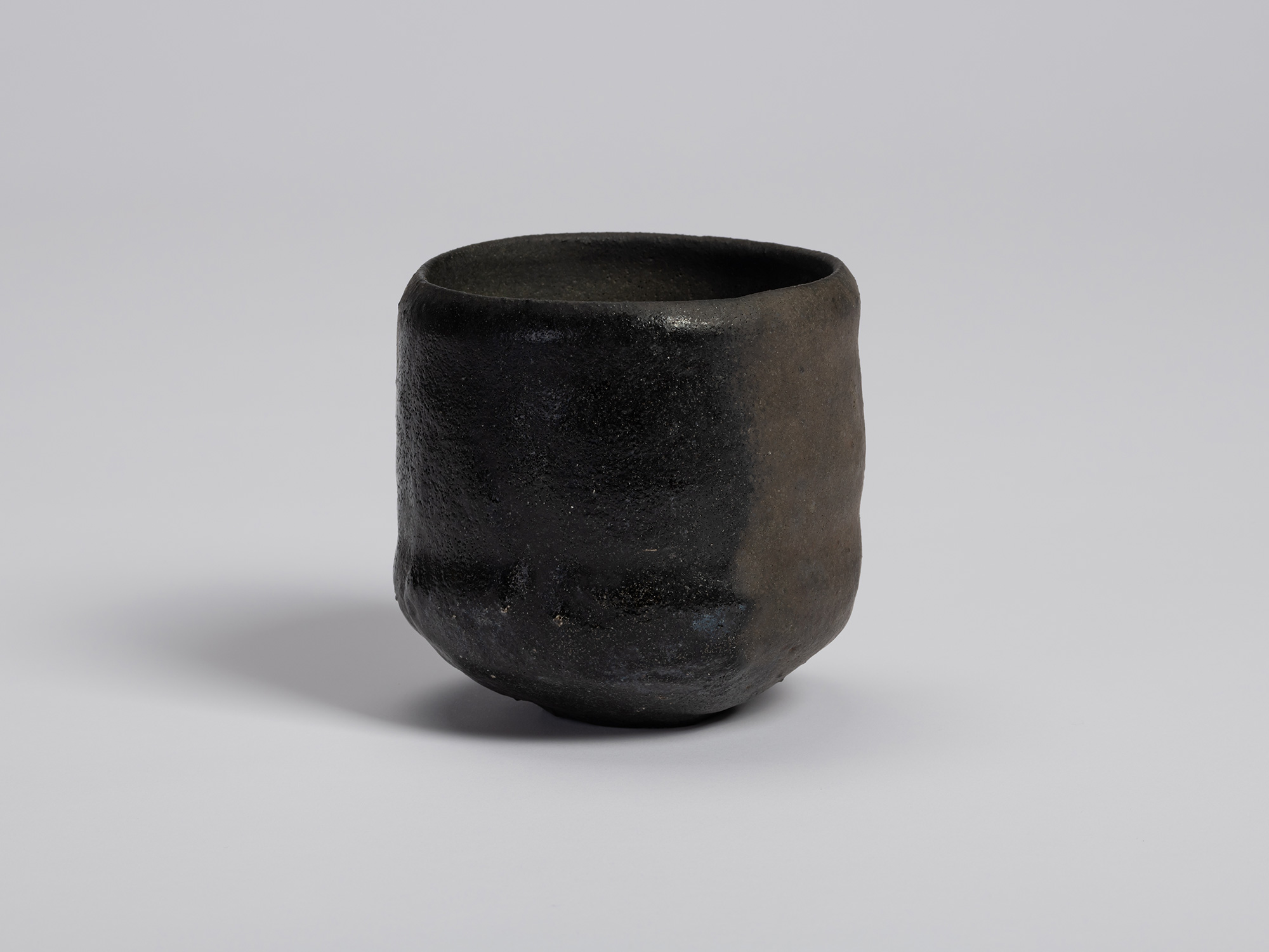 View of a raku-style tea bowl by Tsujimura. The cylindrical form rises from a small foot and features...