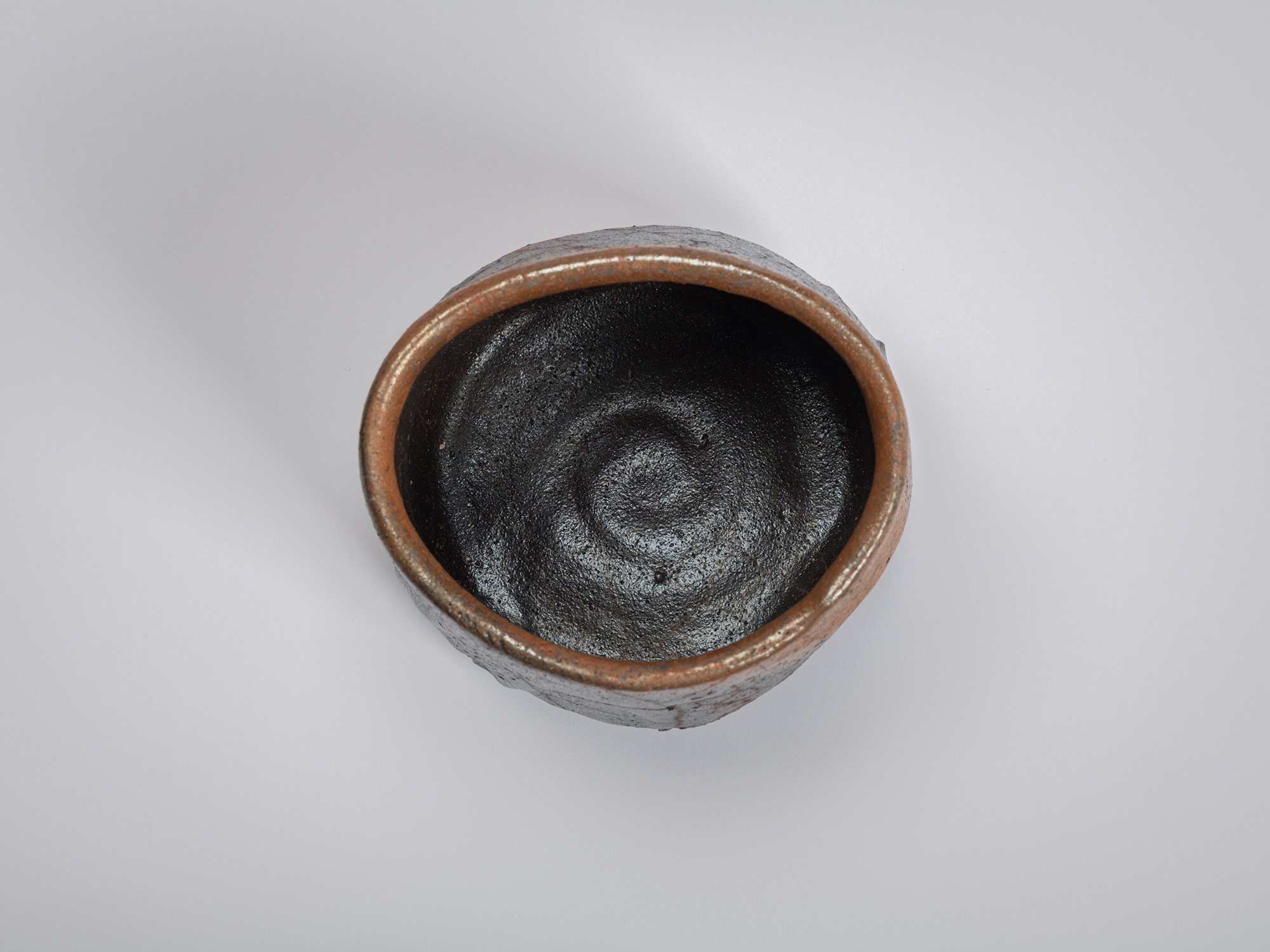 Overhead view of the tea bowl showing a rounded, irregular rim and a dark interior. Concentric...